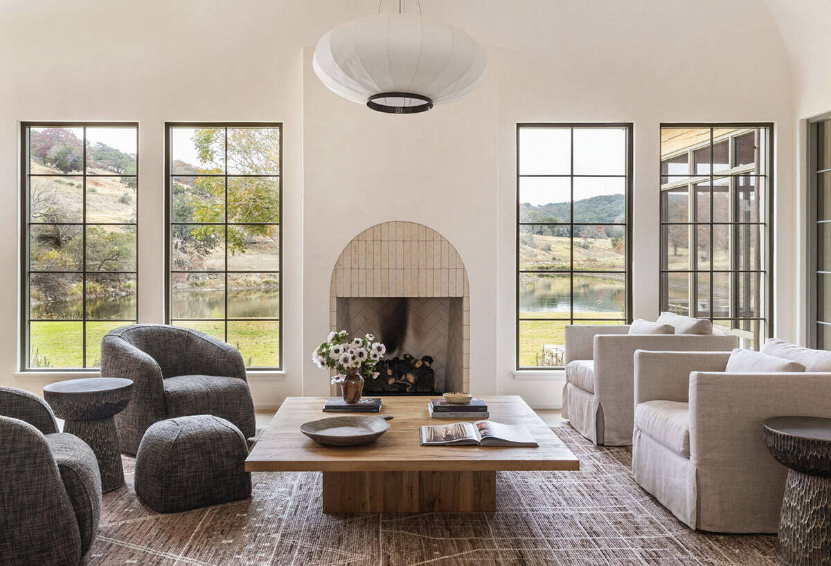 Bright living room with arched travertine fireplace, steel-framed windows overlooking a pond, and oversized paper pendant light