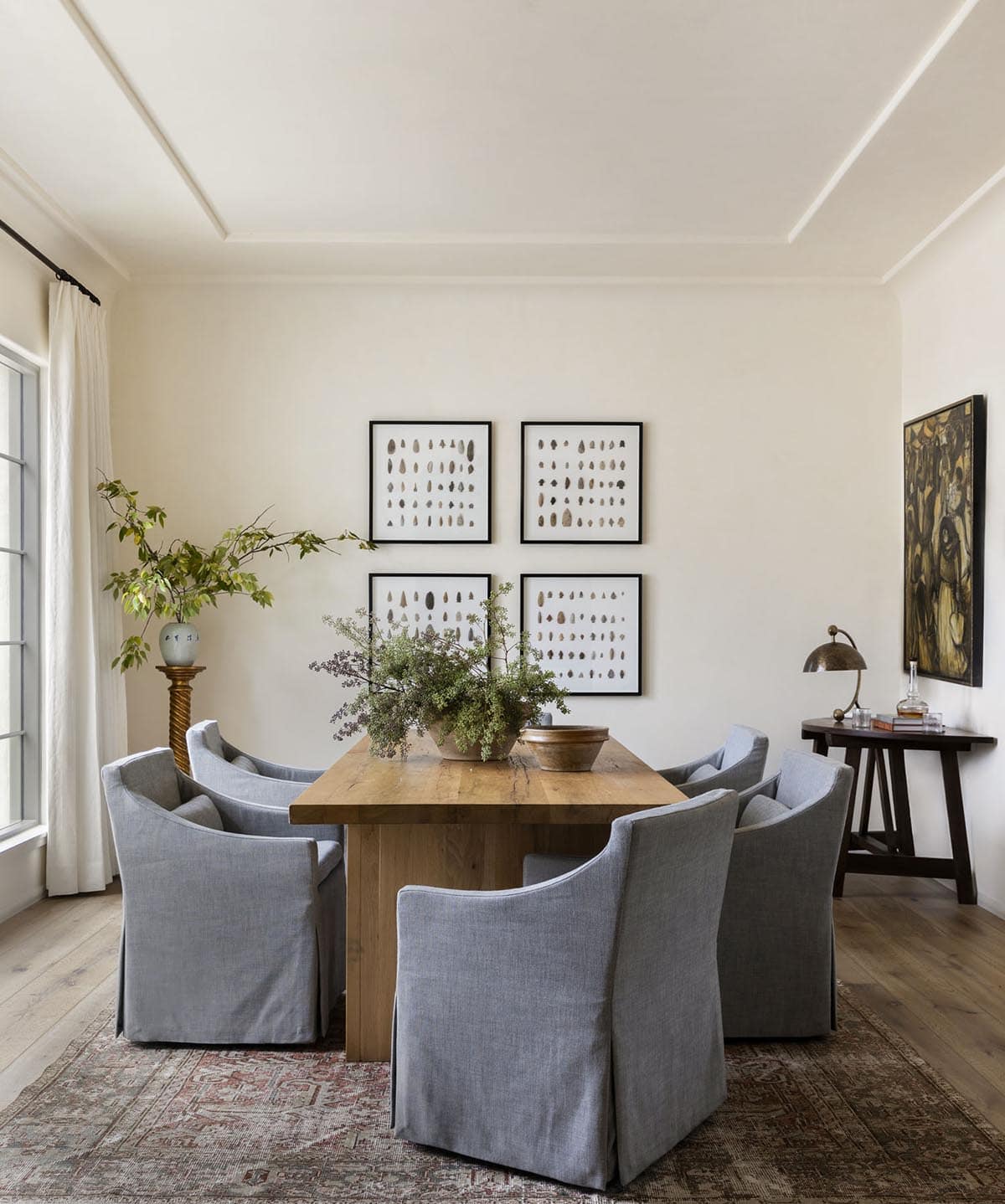 Dining room with oak trestle table, gray slipcovered chairs, arrowhead specimen art grid, and tray ceiling