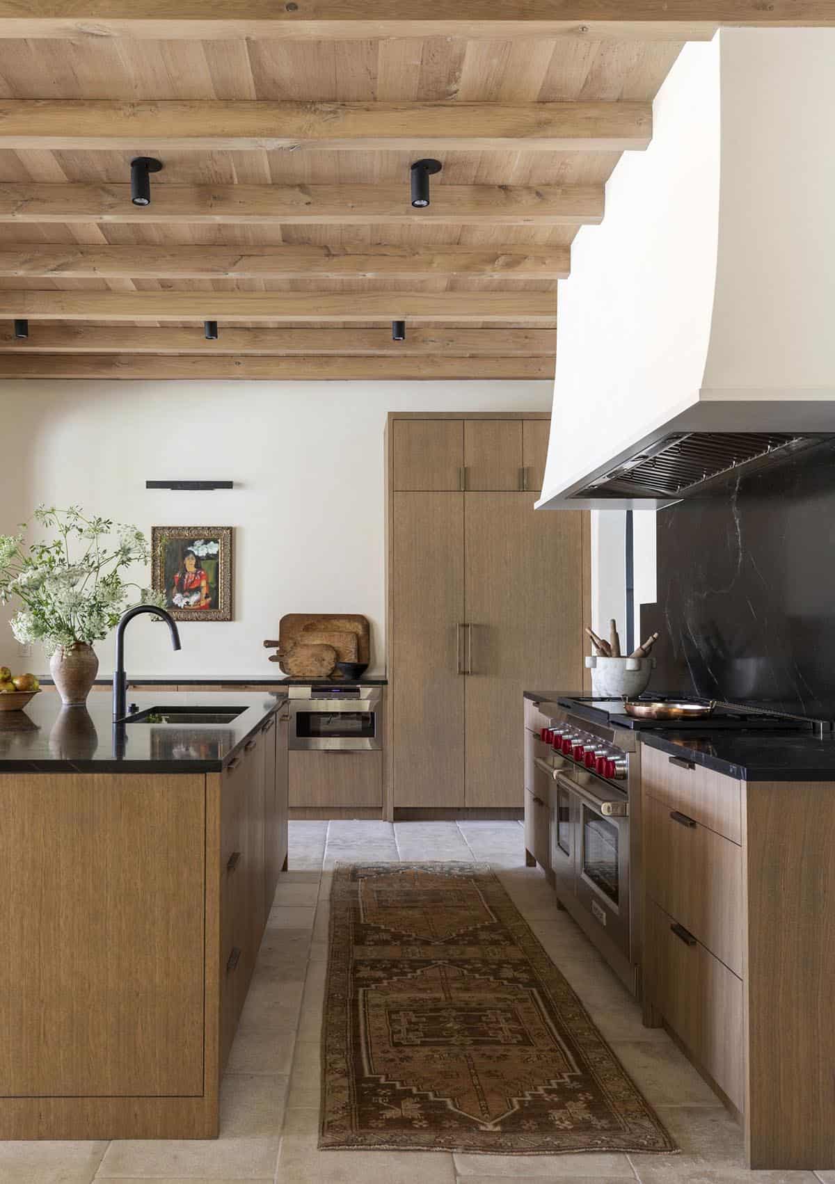 Kitchen detail with wood beam ceiling, black countertops, professional range, and vintage runner rug