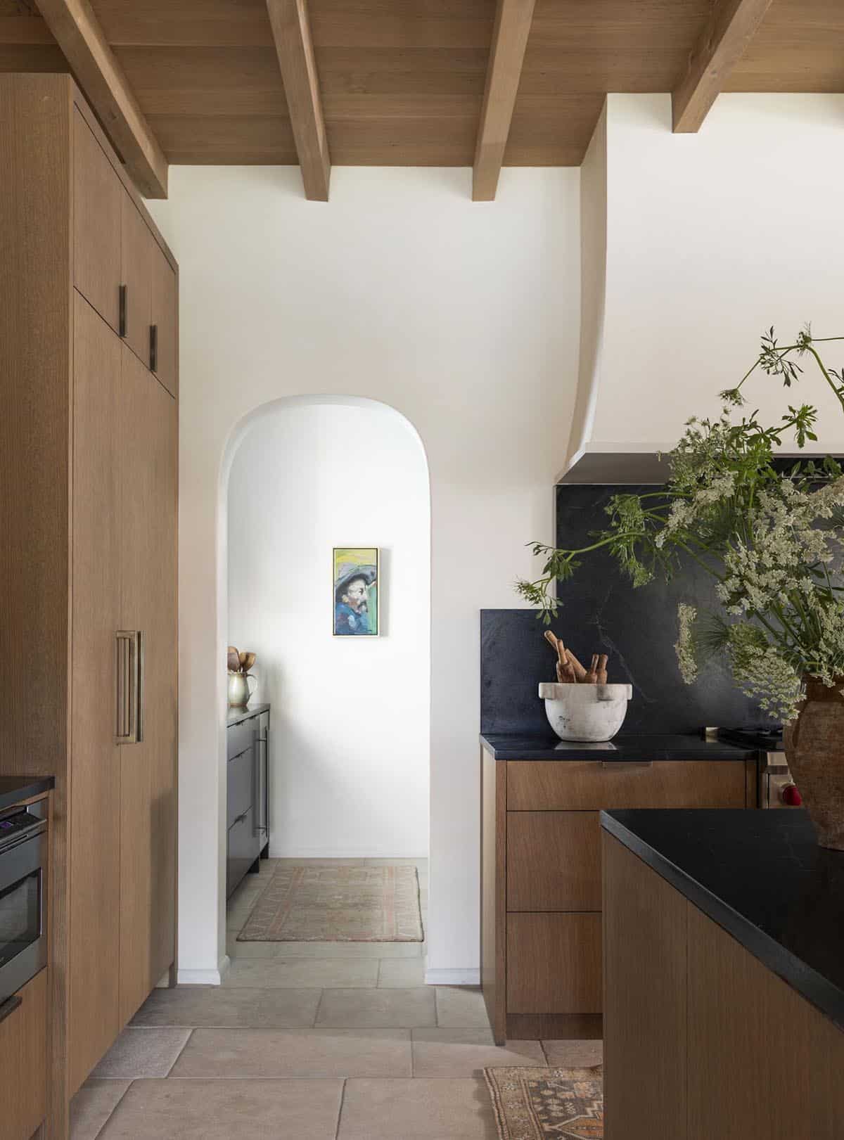 Kitchen arched pass-through leading to butler's pantry with wood cabinetry and black stone counters