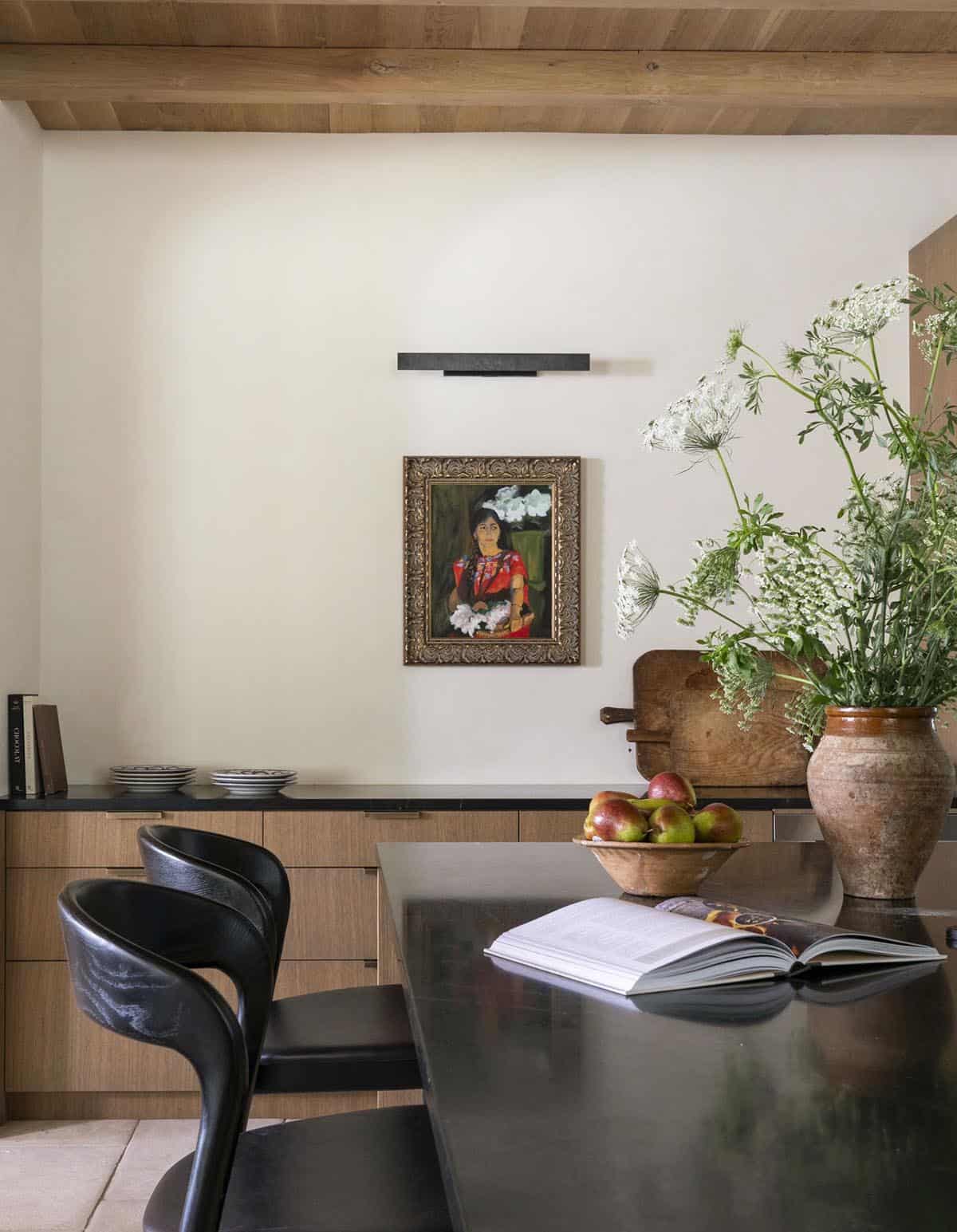 Kitchen nook with dark dining table, black sculptural chairs, ornate framed portrait, and oversized floral arrangement