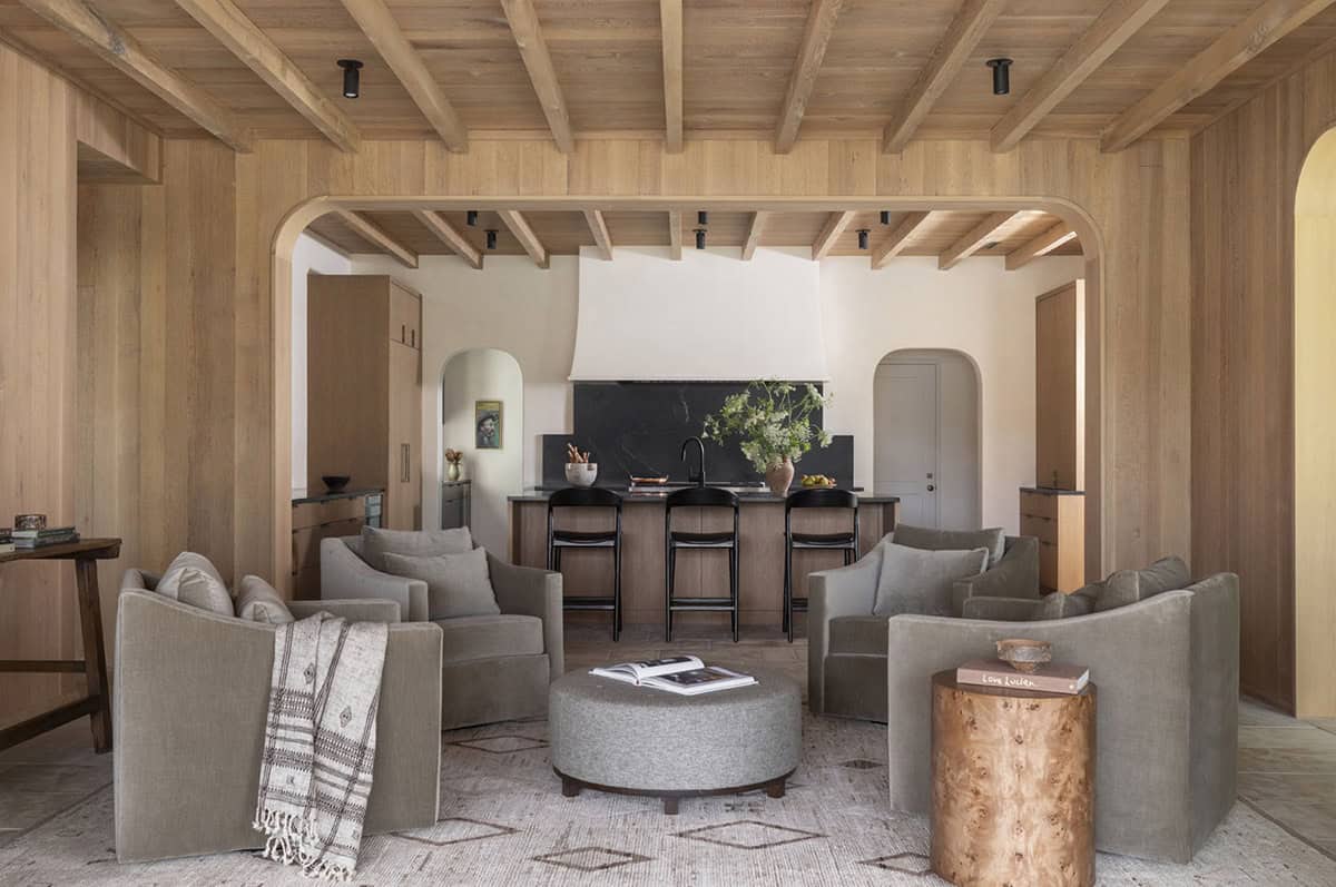 Family room with gray linen swivel chairs, round ottoman, and open view into kitchen through arched opening