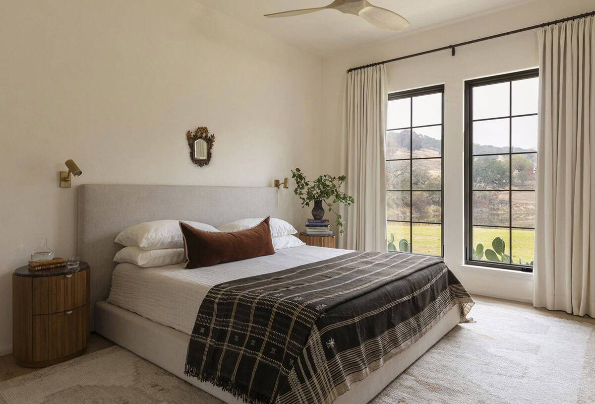 Primary bedroom with upholstered headboard, rust lumbar pillow, steel-framed windows, and Hill Country views