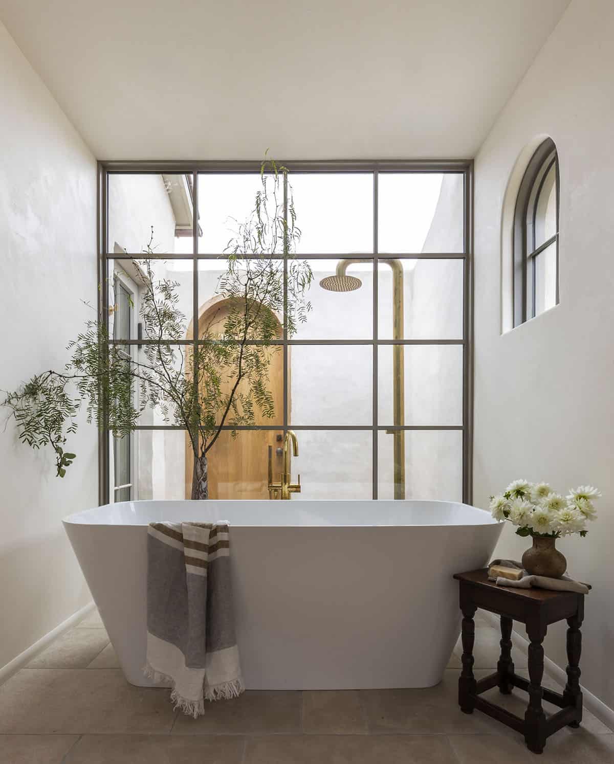 Freestanding soaking tub before steel-framed window overlooking private outdoor shower courtyard