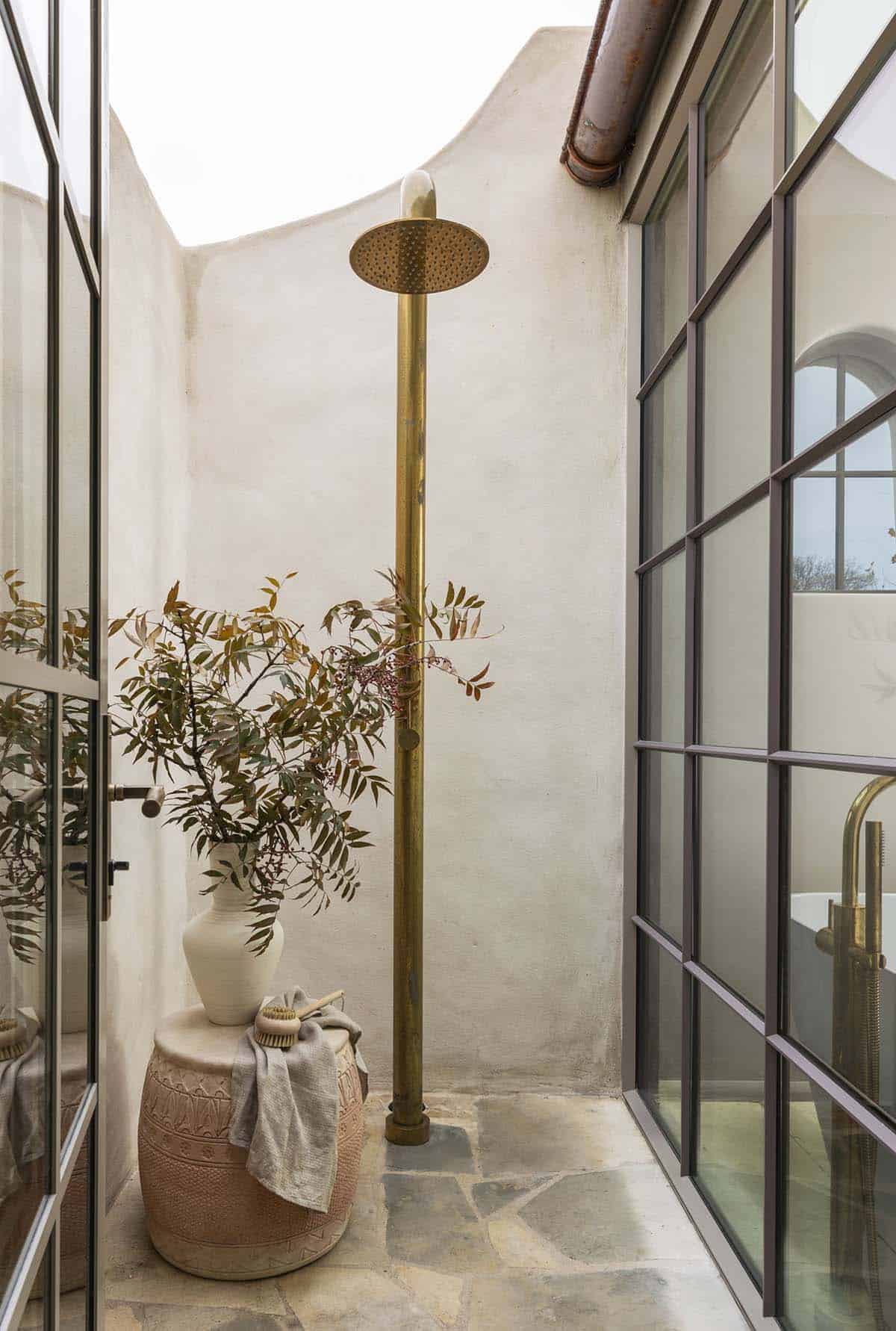 Private outdoor shower courtyard with brass rainfall fixture, flagstone floor, and plaster walls