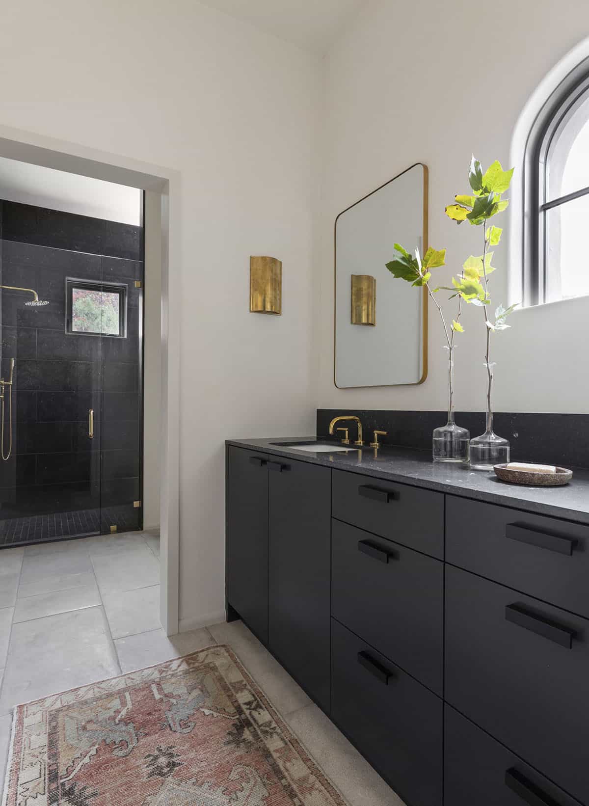 Secondary bathroom with matte black vanity, black granite countertop, brass sconces, and all-black tiled shower