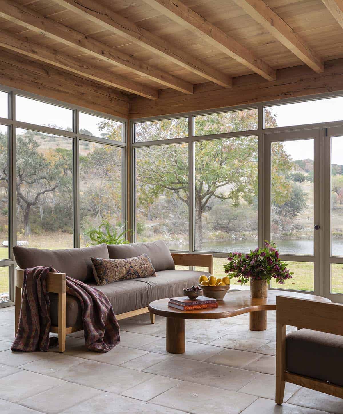 Sunroom detail with linen sofa, vintage kilim lumbar pillow, sculptural wood coffee table, and Hill Country landscape views
