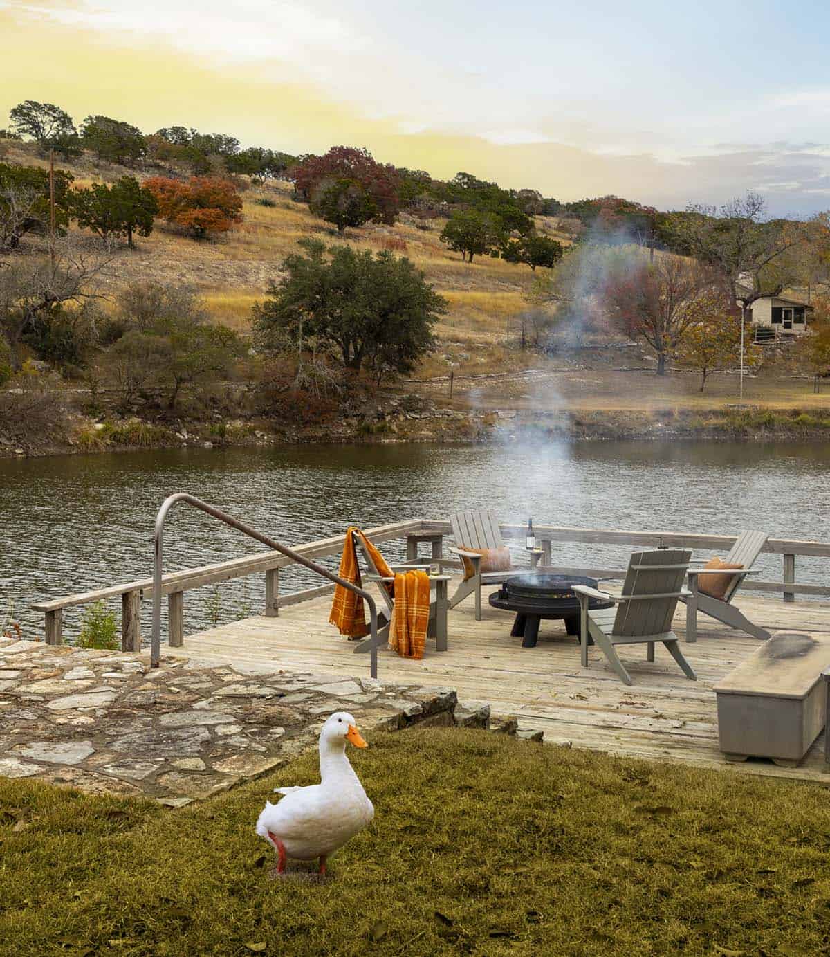 White duck on flagstone path leading to lakeside dock with Adirondack chairs and smoking fire pit