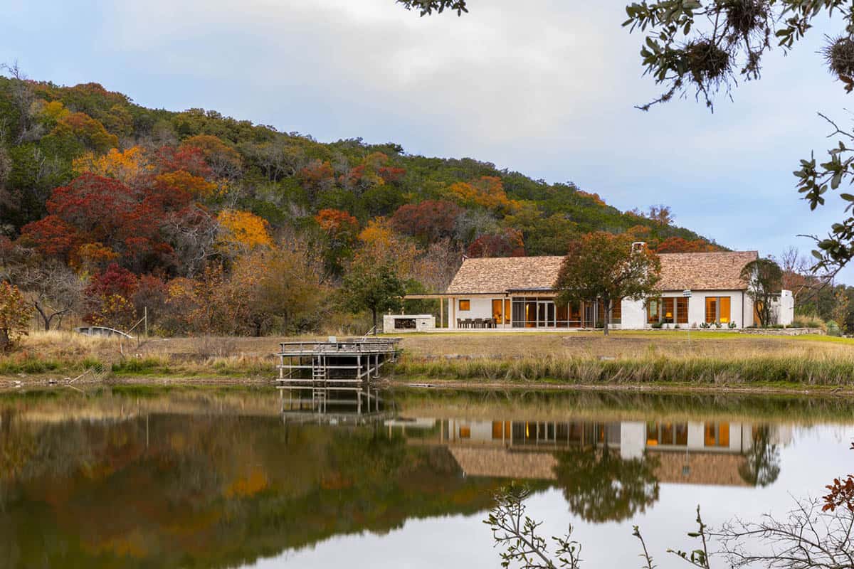 White stucco hacienda reflected in still pond surrounded by vibrant fall foliage and wooded hills