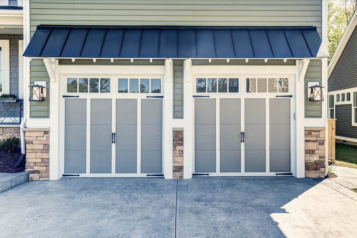 Two-car garage with gray carriage-style doors, black metal roof overhang, and stone base accents