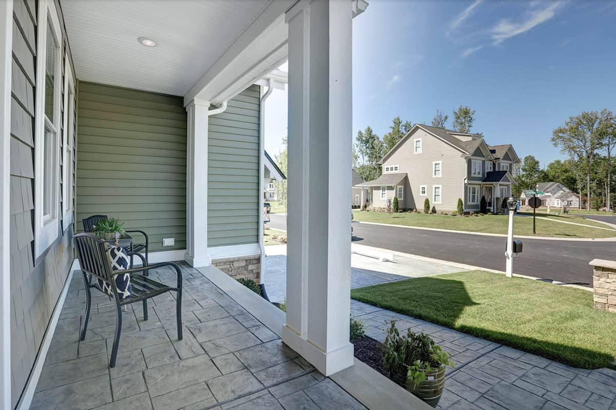 Covered front porch with stamped concrete floor, white columns, and black metal chairs overlooking a suburban street