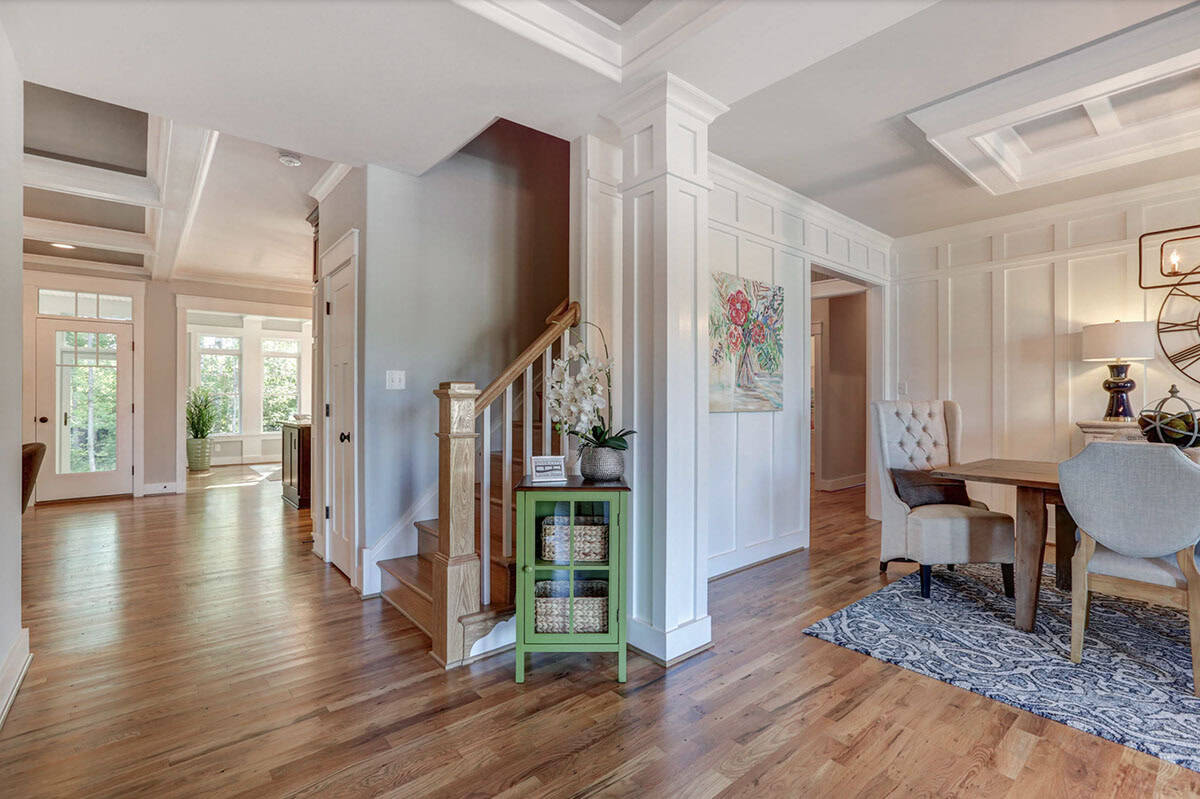 Open foyer with wood staircase, hardwood floors, coffered ceiling, and view into dining room