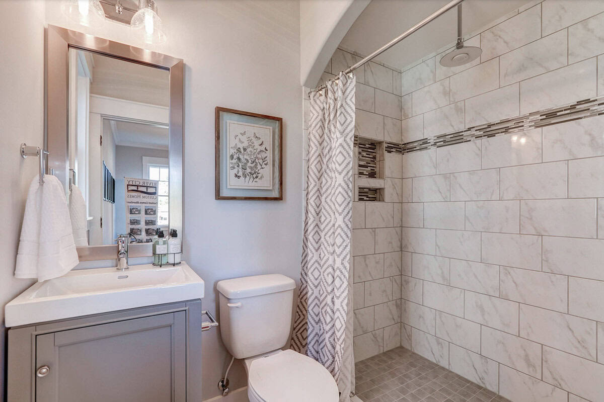 Full bathroom with gray vanity, marble-look subway tile walk-in shower, and rain showerhead
