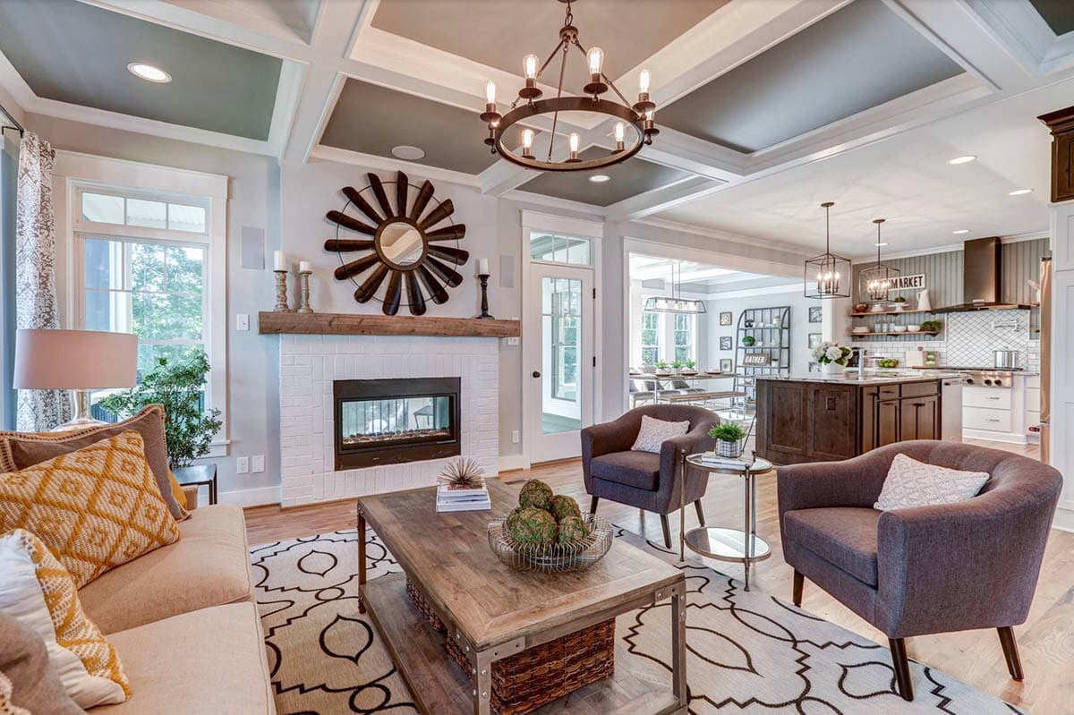 Open-plan living room and kitchen with coffered ceiling, ring chandelier, fireplace, and dark wood island