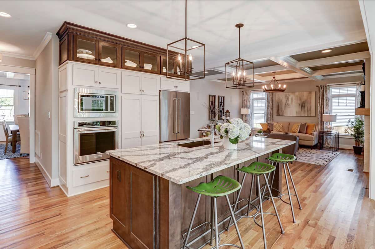 Kitchen island with granite countertop and green barstools, open to living room beyond