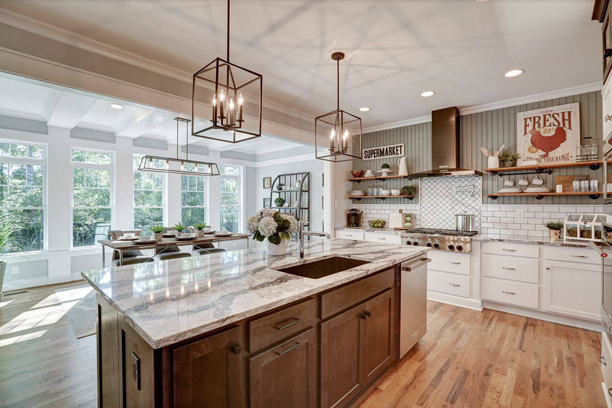 Large kitchen island with granite countertop and farmhouse sink, open to bright breakfast nook and cooking wall with open shelving