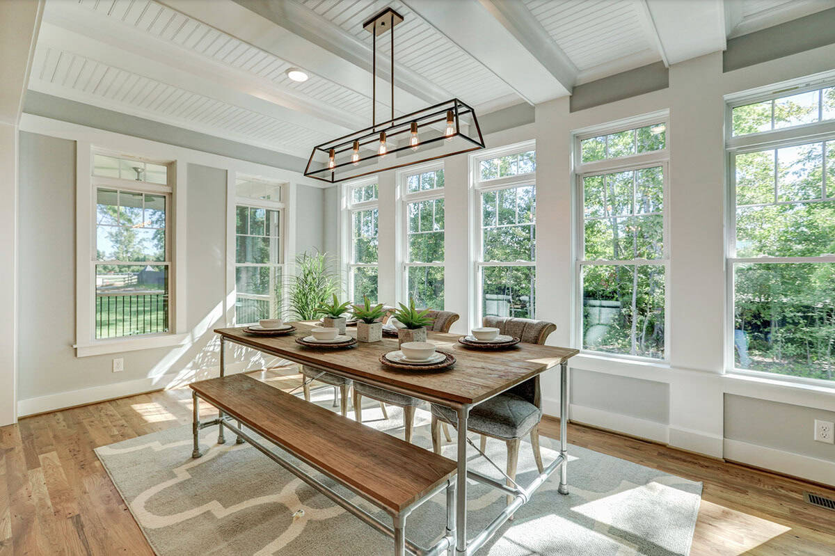 Sun-filled farmhouse breakfast nook with industrial pipe table, bench, and wraparound windows overlooking backyard