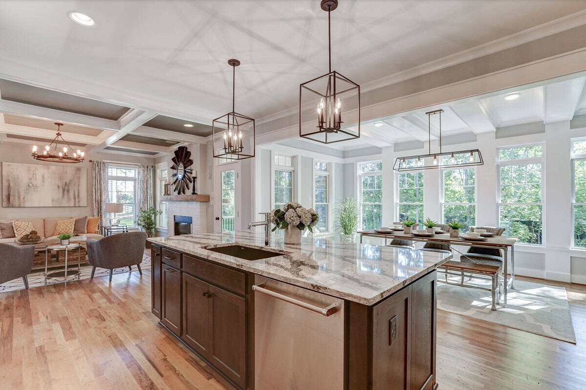 Open-plan kitchen and living area viewed from island, showing coffered ceilings, fireplace, and breakfast nook beyond