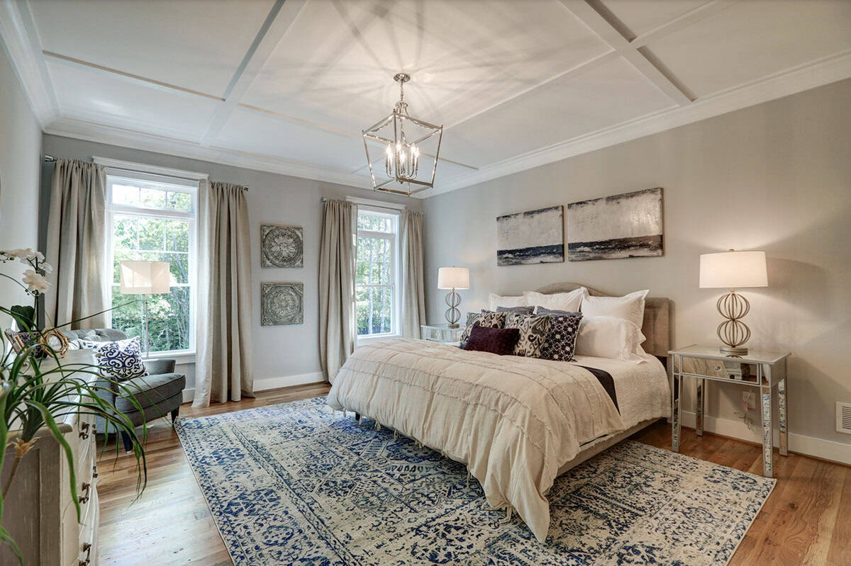 Primary bedroom with coffered ceiling, silver lantern chandelier, upholstered headboard, and blue patterned area rug