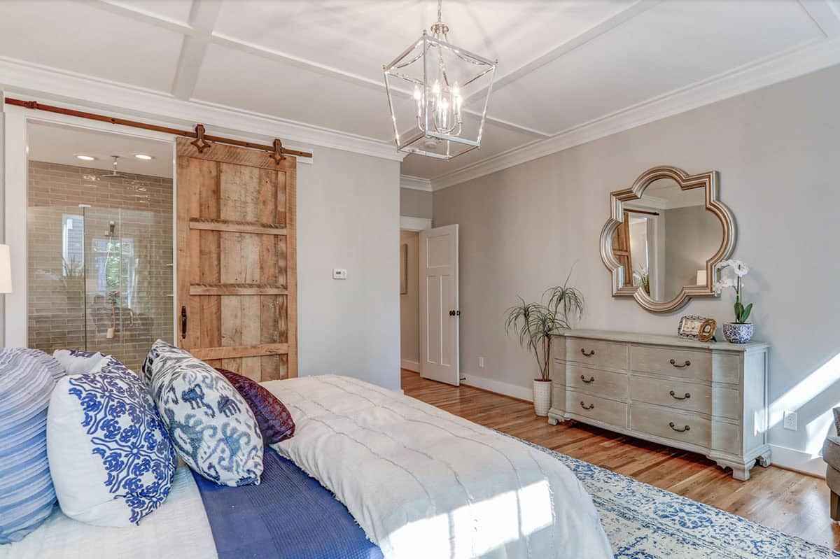 Primary bedroom with barn door to ensuite, gray dresser with quatrefoil mirror, and blue accent bedding