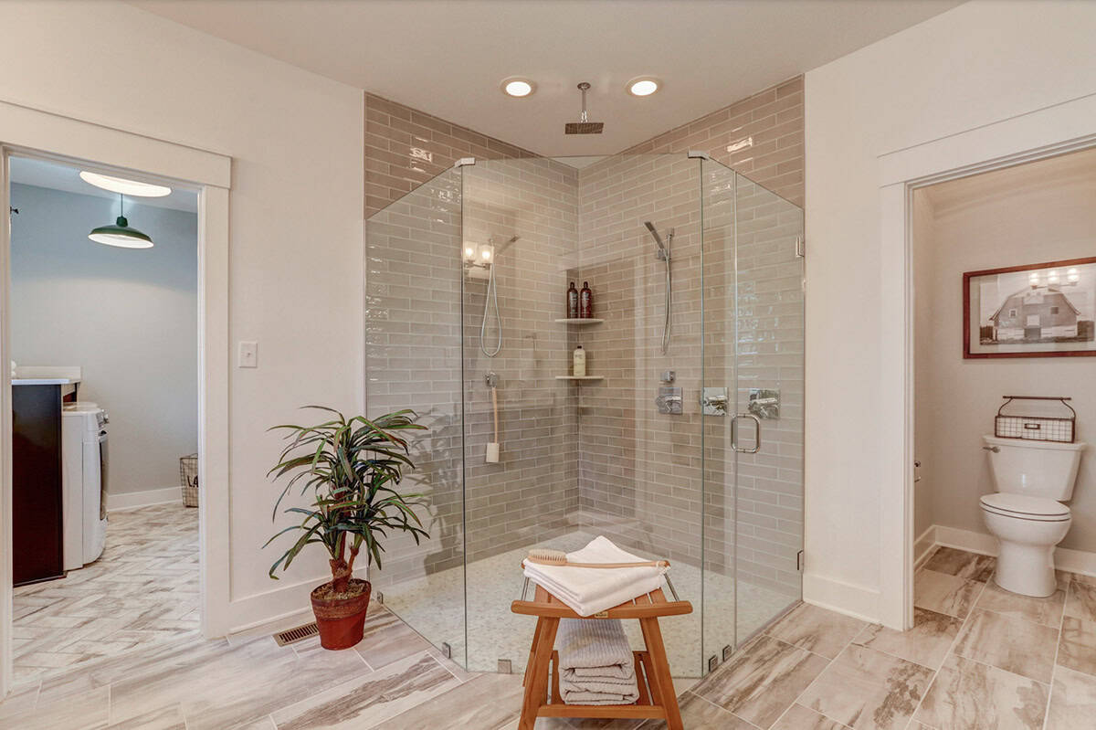 Primary ensuite with large frameless glass corner shower, gray subway tile, and doorway to laundry room
