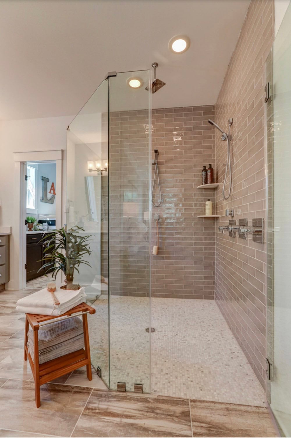 Primary ensuite frameless glass walk-in shower with gray subway tile walls and rain showerhead