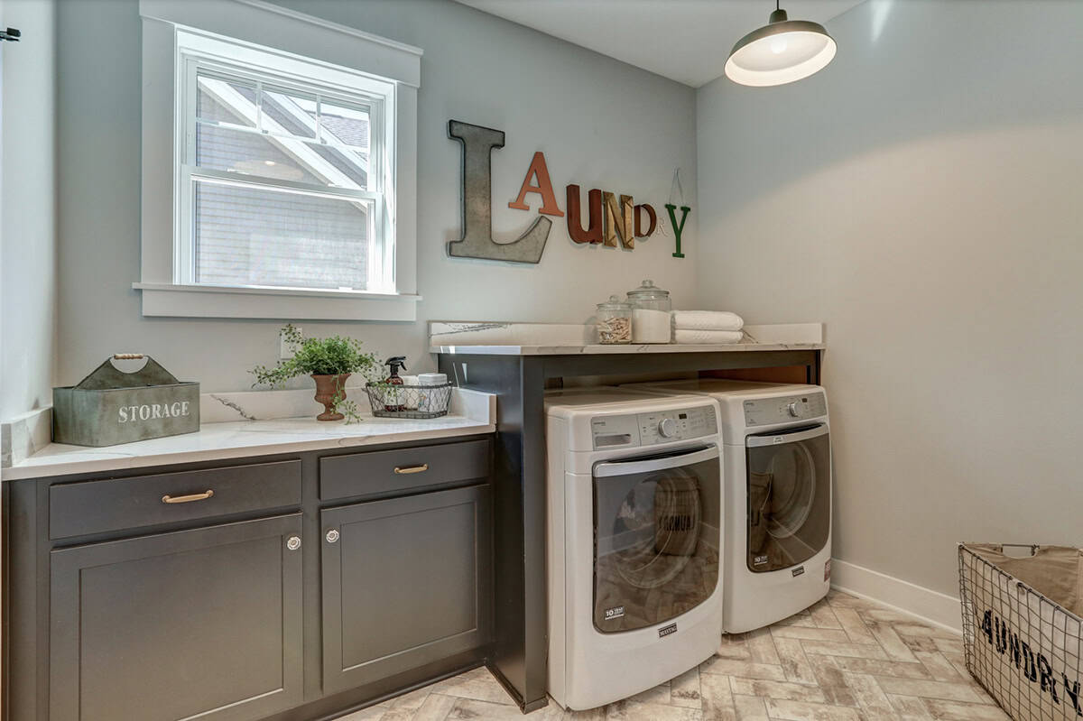 Laundry room with gray cabinets, marble countertop, front-load washer and dryer, and decorative letter signage