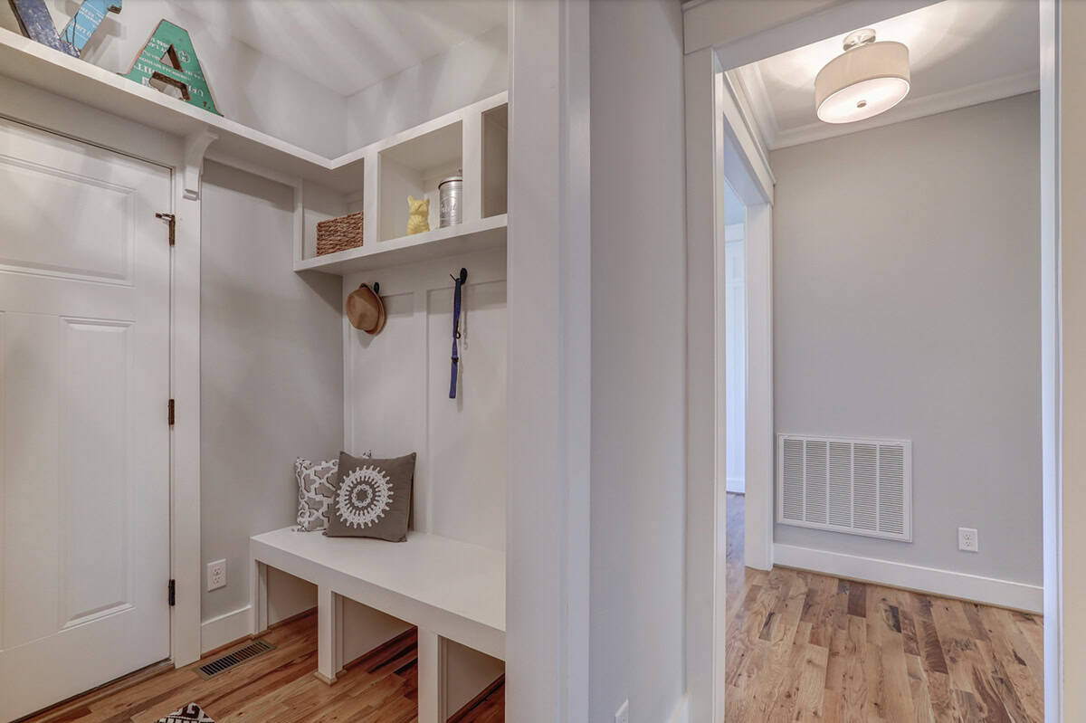 Mudroom with built-in white bench, upper cubbies, wall hooks, and hardwood floors