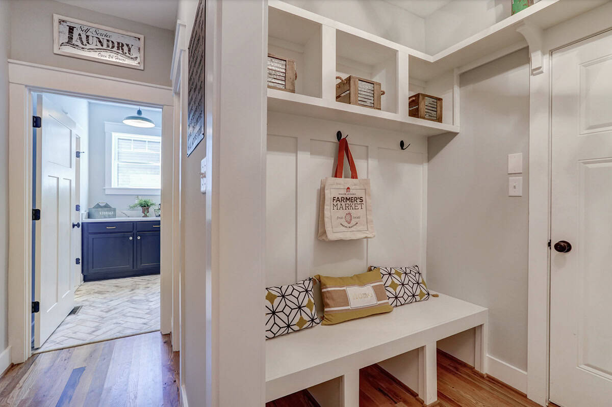 Mudroom with built-in white bench and upper cubbies, opening to blue-cabinet laundry room beyond