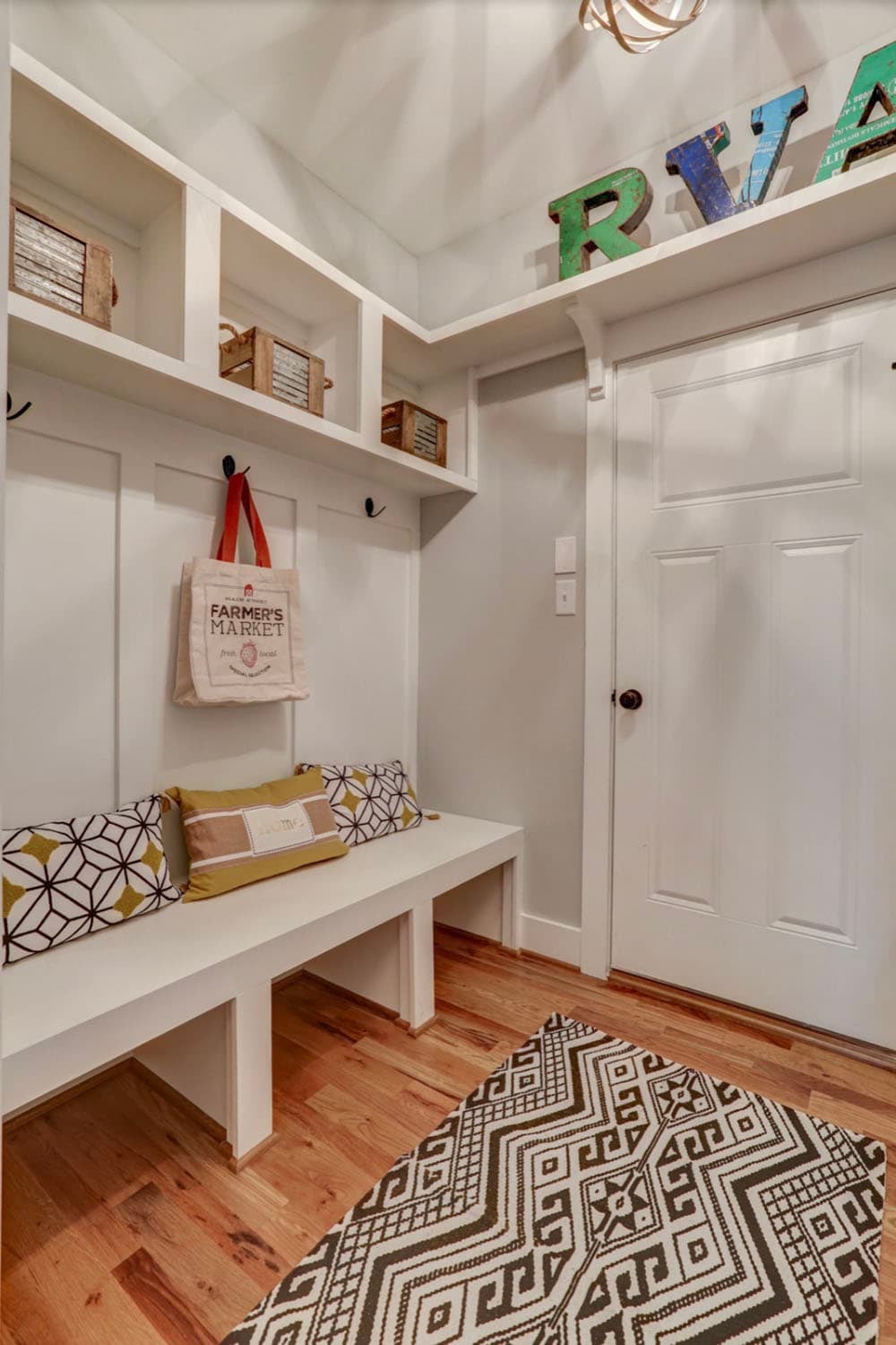 Mudroom with built-in bench, upper storage cubbies, wall hooks, and colorful RVA letter display on top shelf