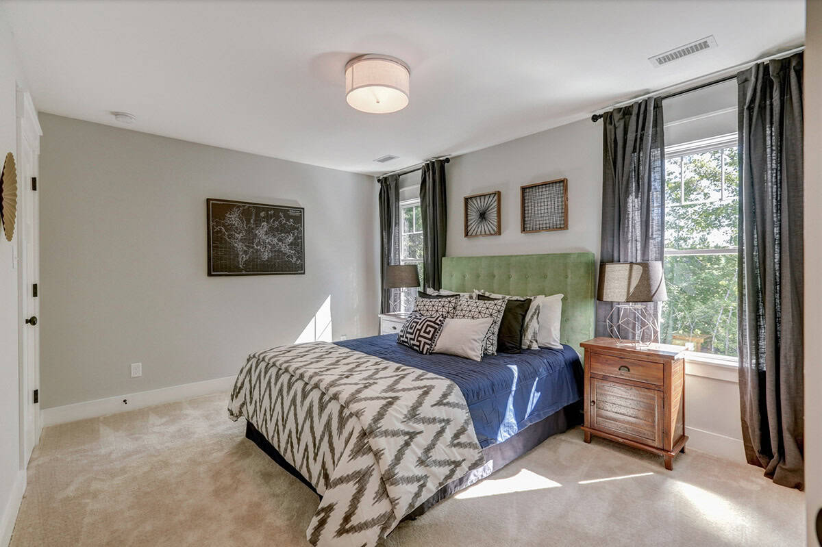 Secondary bedroom with green tufted headboard, blue accent bedding, world map wall art, and gray curtains