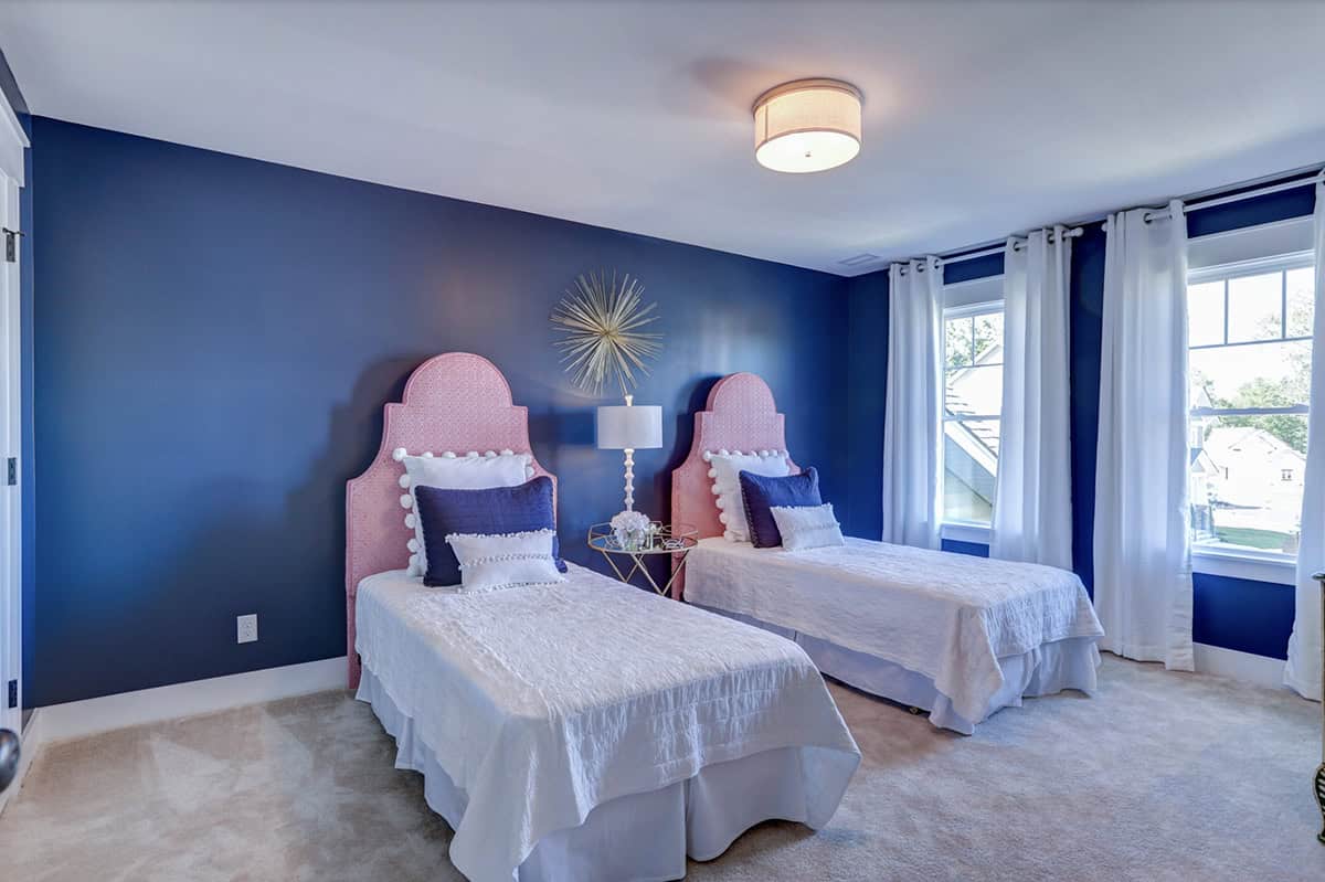 Girls bedroom with navy blue accent walls, twin pink upholstered headboards, and gold starburst wall decor