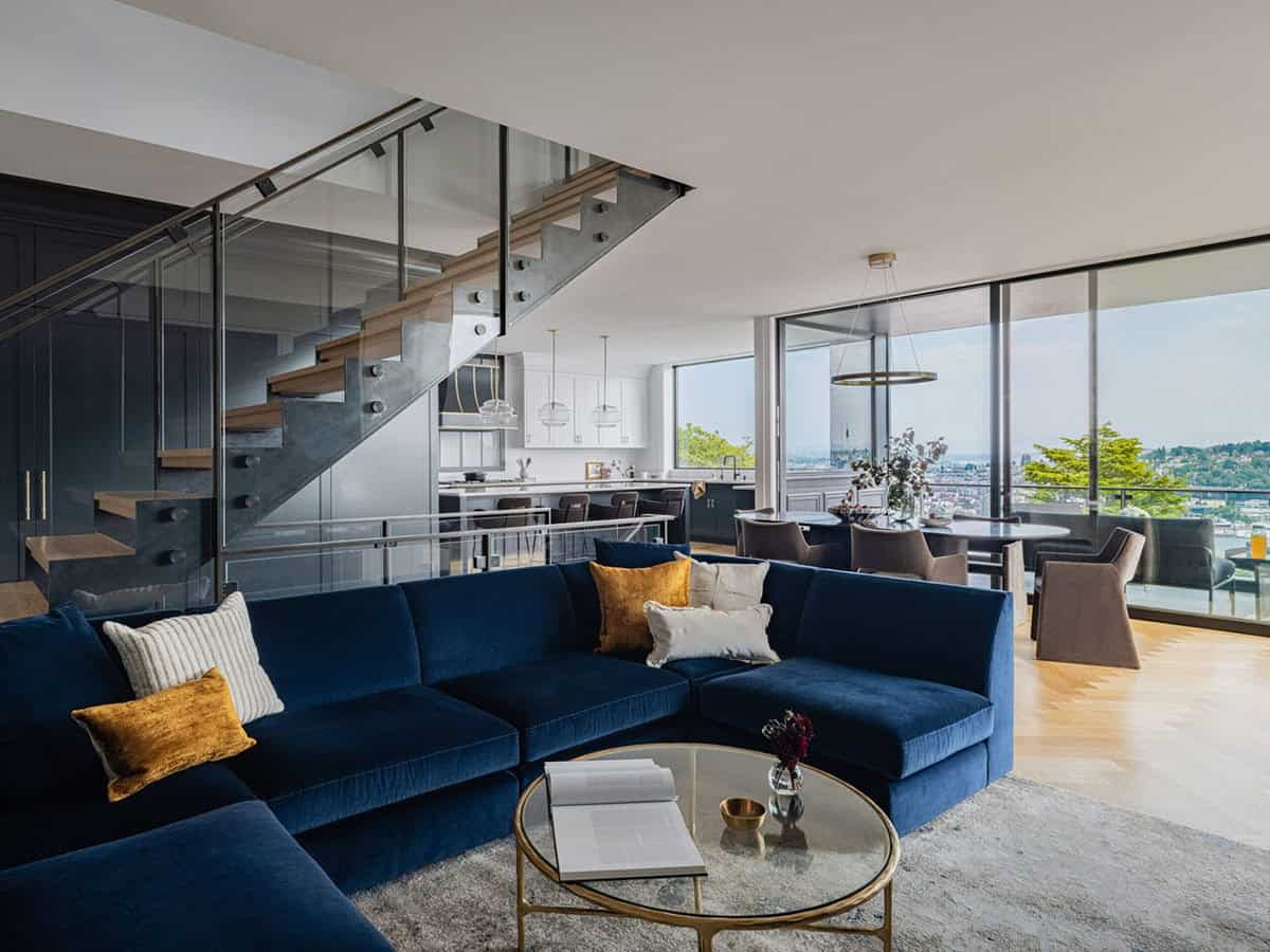 Open-plan living area with navy sectional, floating staircase, kitchen, and panoramic city views