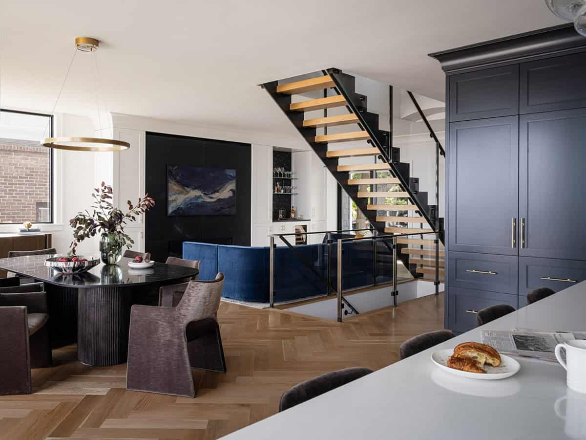 Open-plan dining and living space with floating staircase, navy cabinetry, and herringbone floors