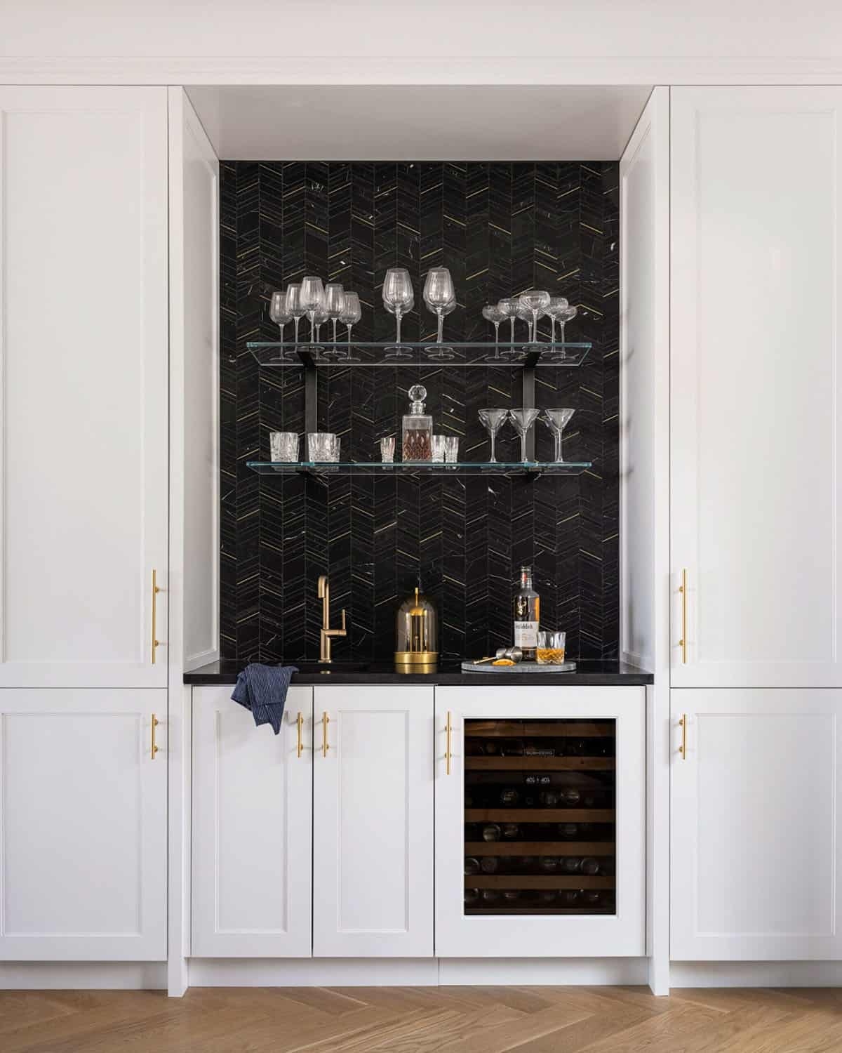 Built-in bar niche with black chevron marble backsplash, glass shelves, and wine refrigerator
