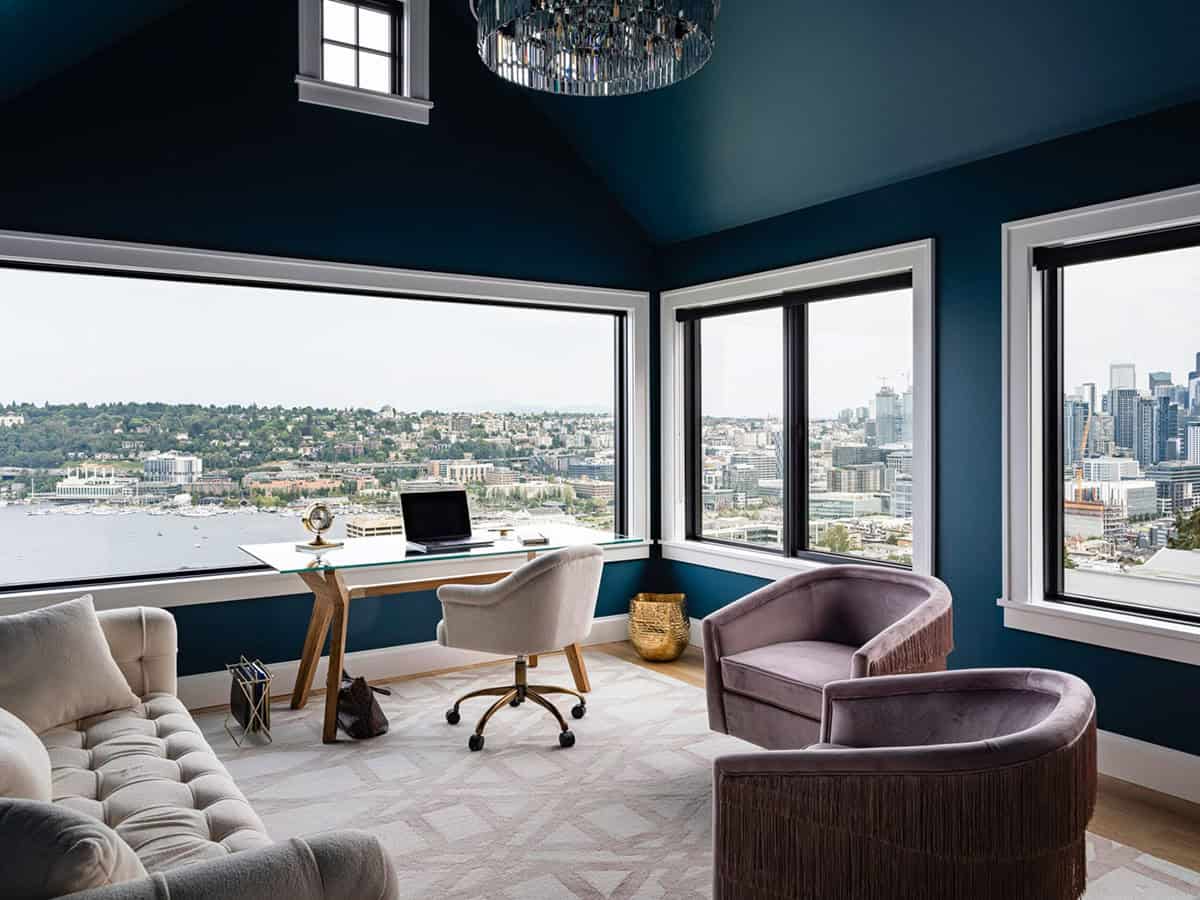 Home office with deep teal walls, wraparound windows, city and water views, and crystal chandelier