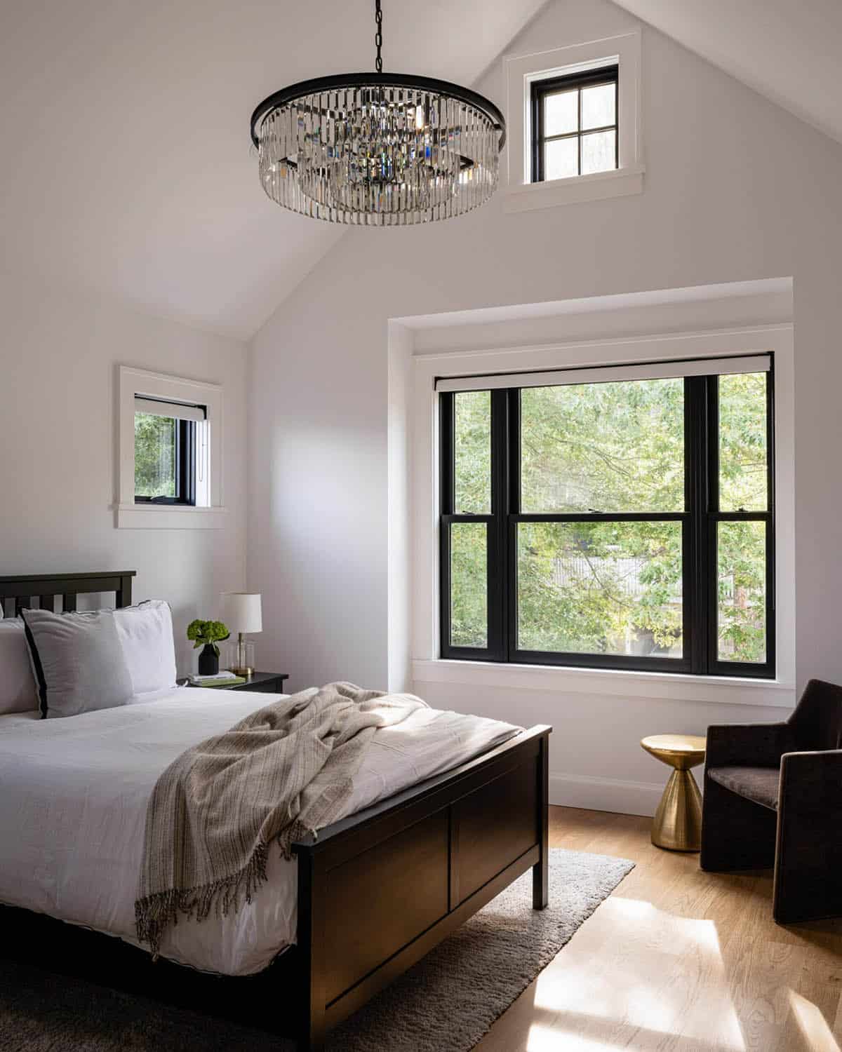 Bedroom with vaulted ceiling, crystal chandelier, black-framed windows, and treetop views