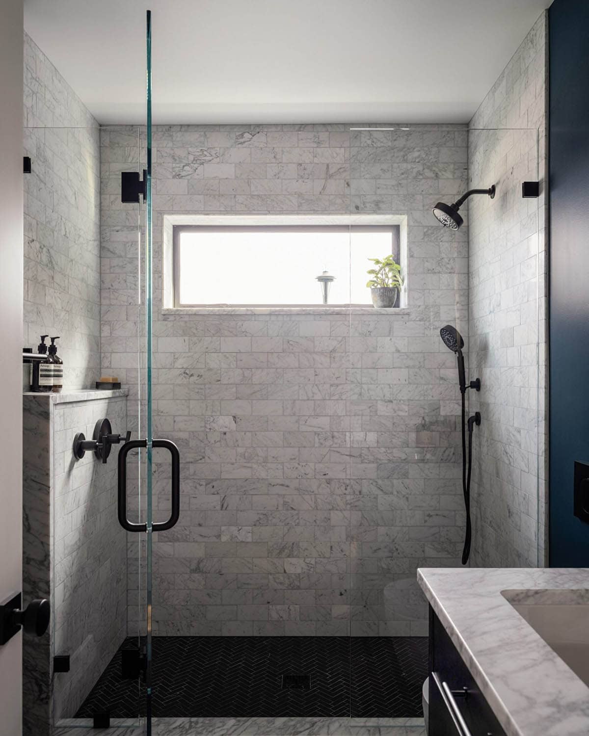 Walk-in shower with marble subway tile walls, black fixtures, and Space Needle visible through window
