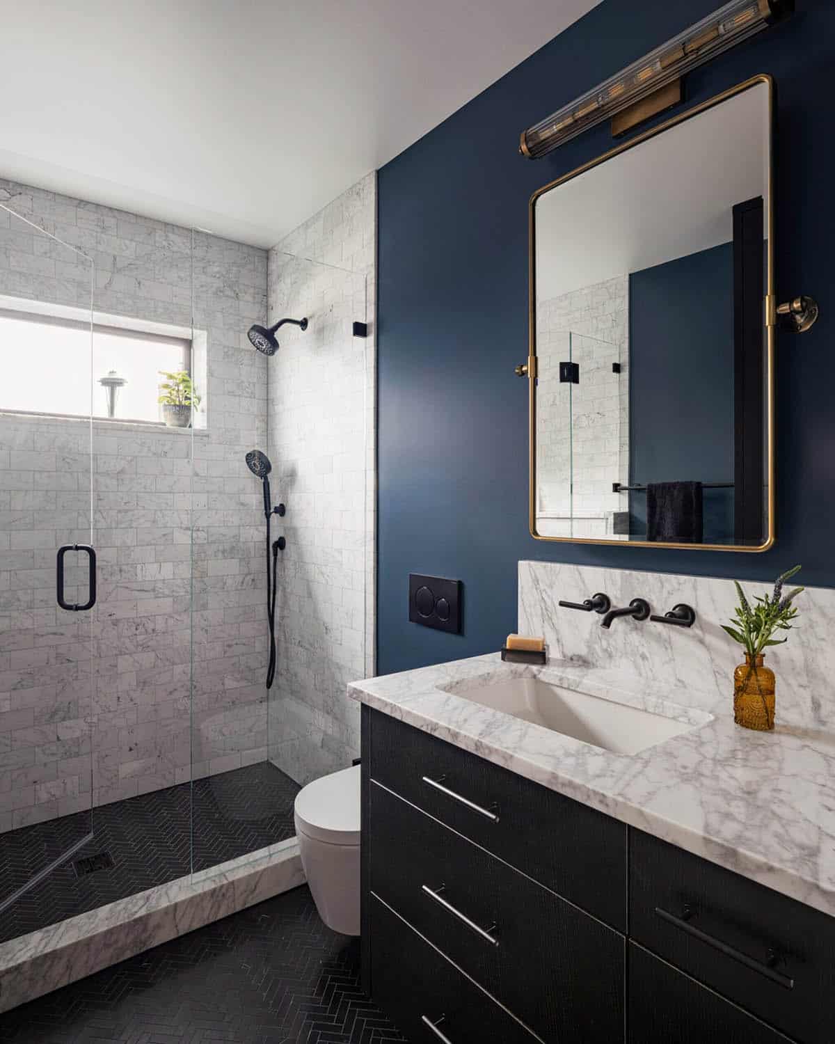 Bathroom with navy accent wall, marble tile shower, dark vanity, and gold-framed mirror