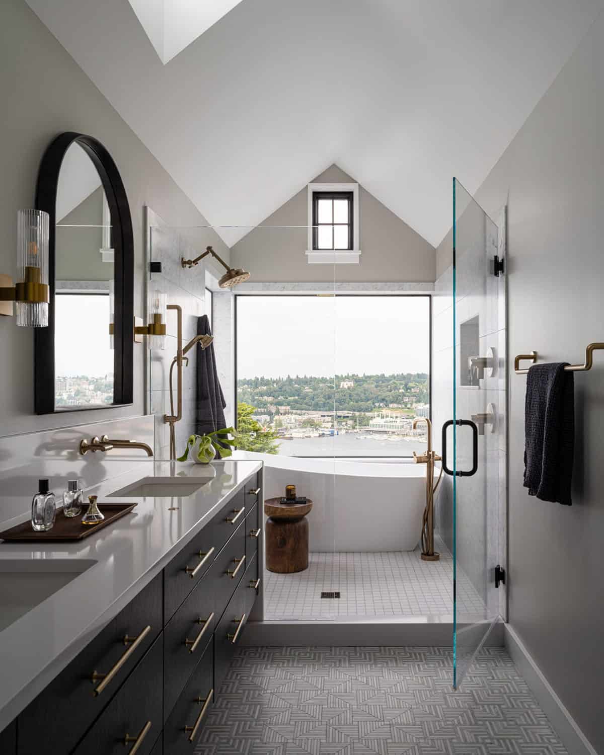 Primary bathroom with vaulted ceiling, freestanding tub, glass shower, brass fixtures, and lake views