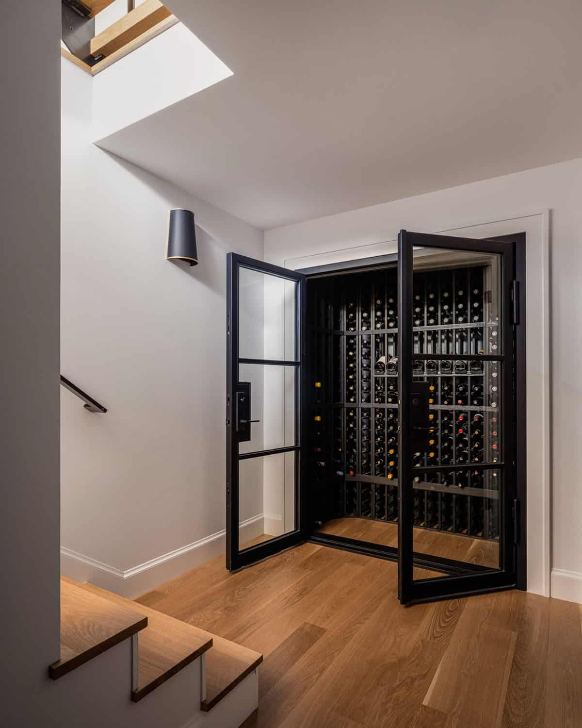 Open double-door wine cellar with black metal racks filled with bottles, viewed from staircase landing