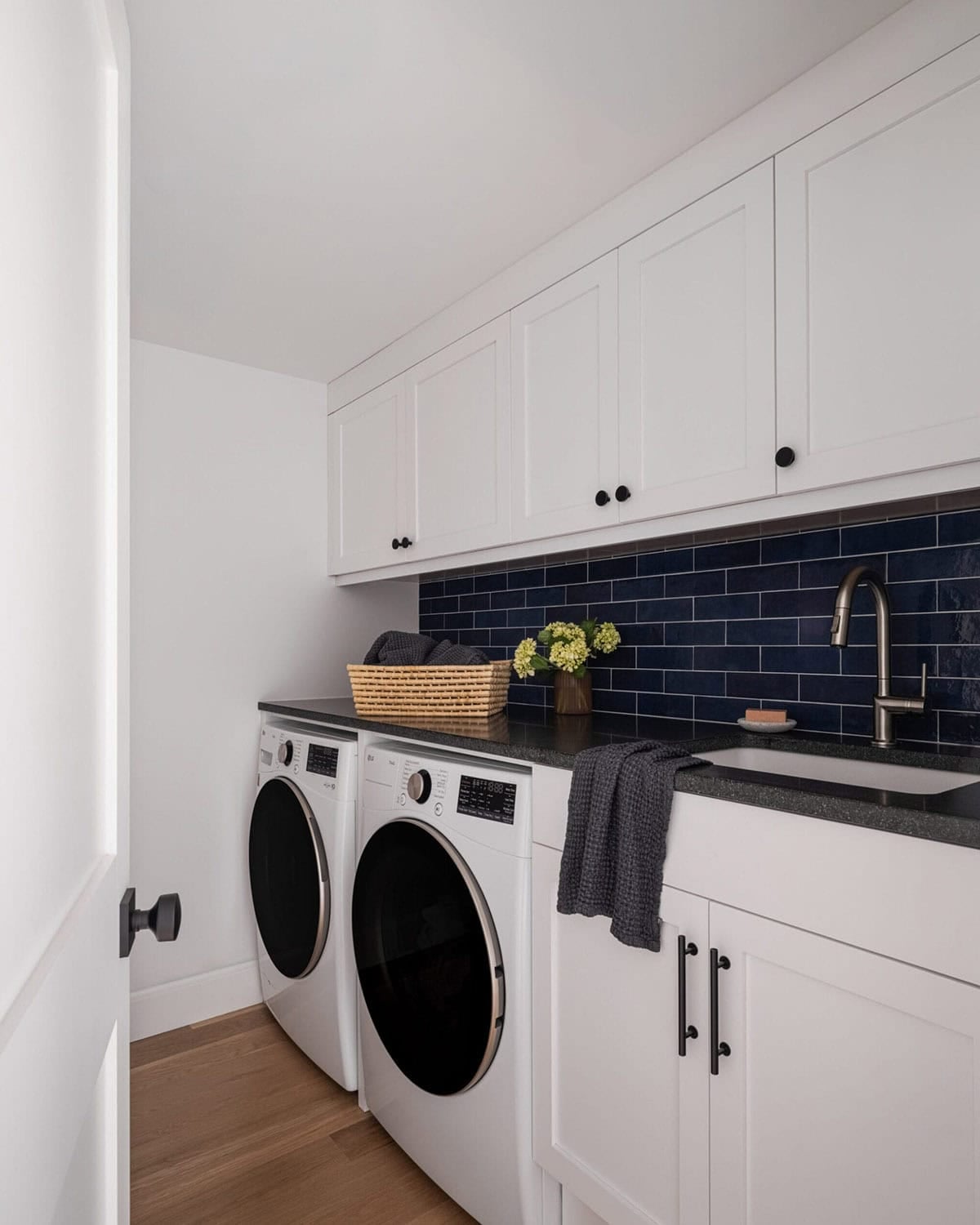 White laundry room with navy subway tile backsplash, front-load washer and dryer, and black hardware