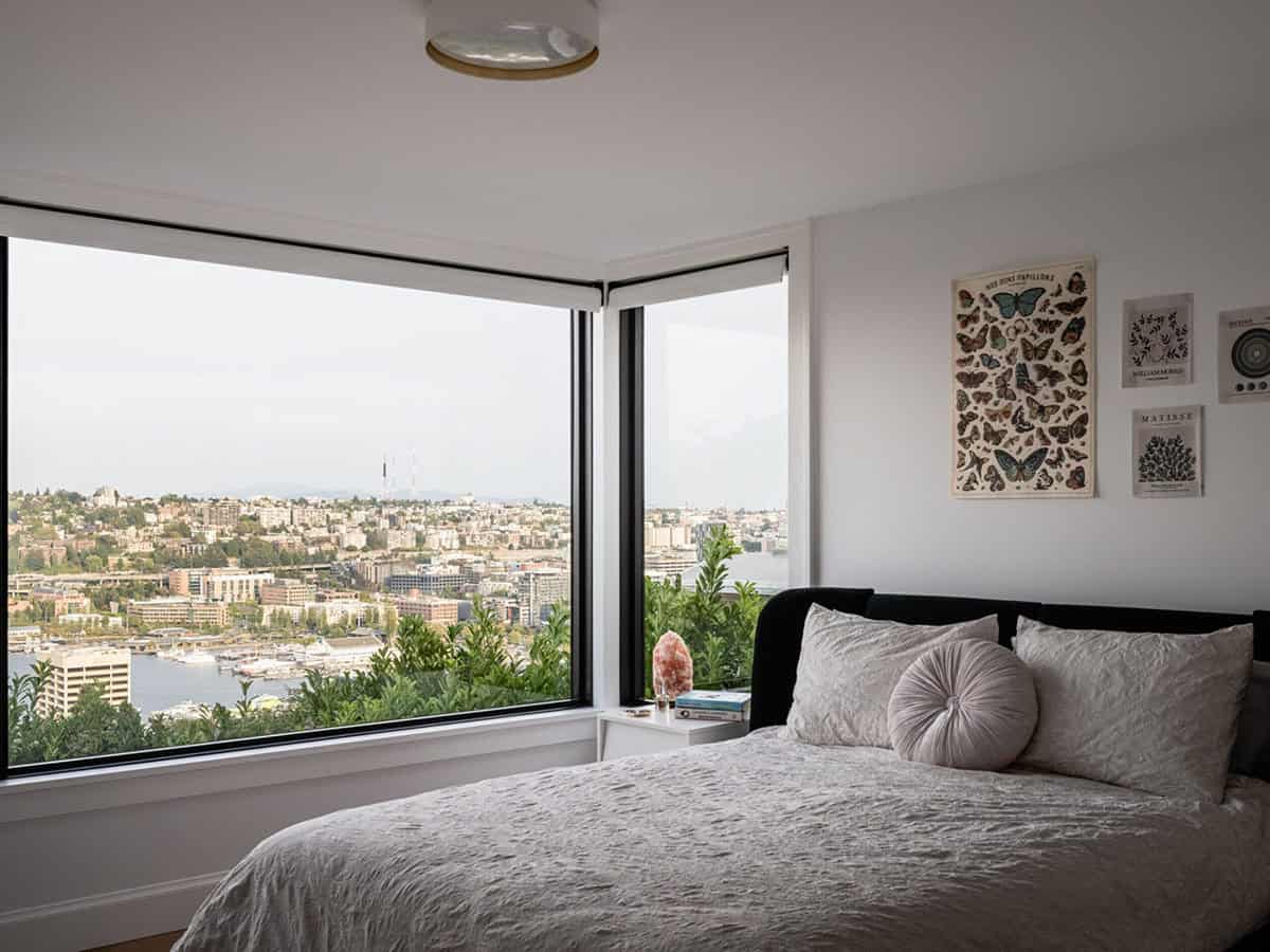 Bright bedroom with corner picture windows, city and water views, and botanical art gallery wall