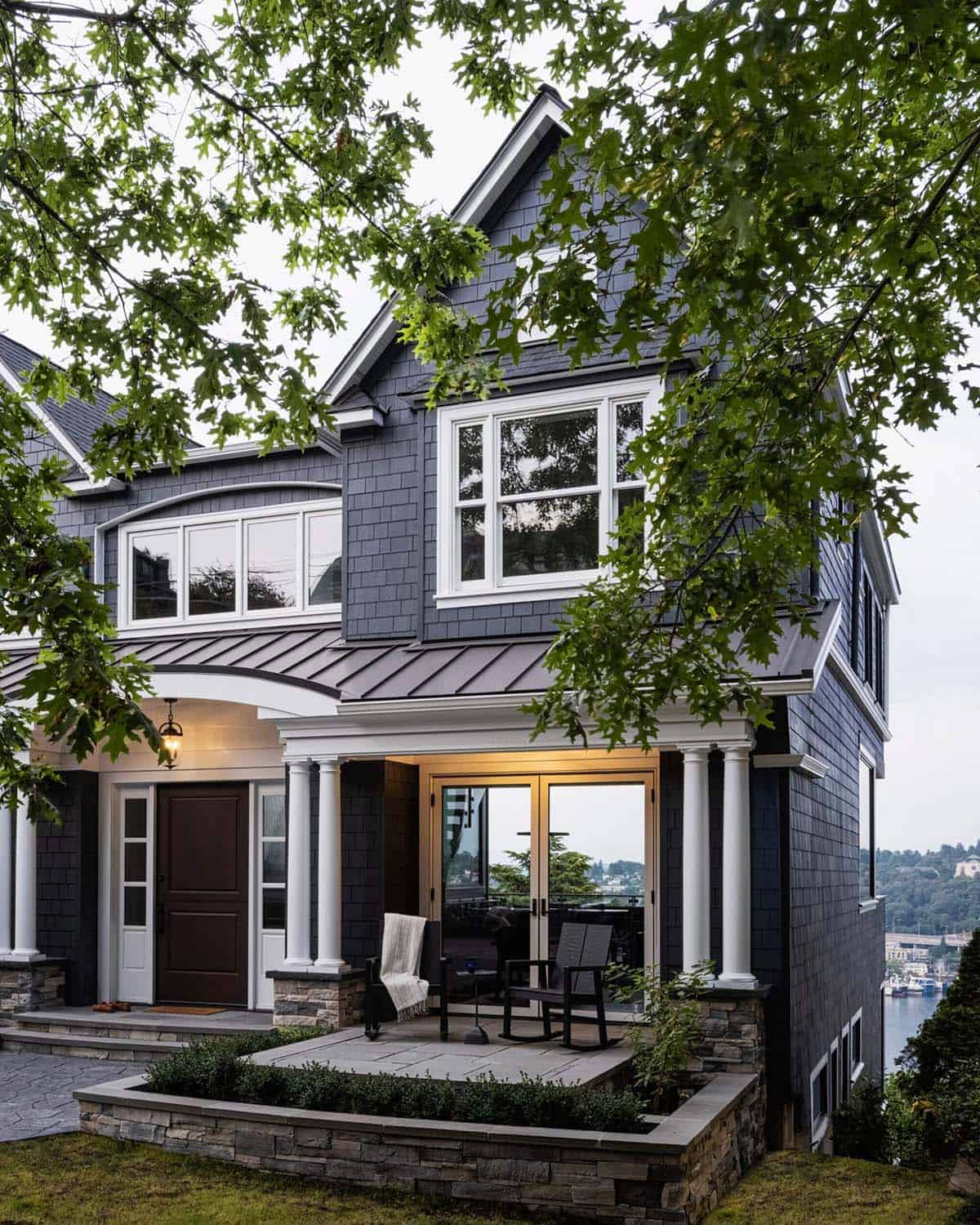 Dark navy craftsman home exterior framed by tree canopy with lit porch and water views at dusk