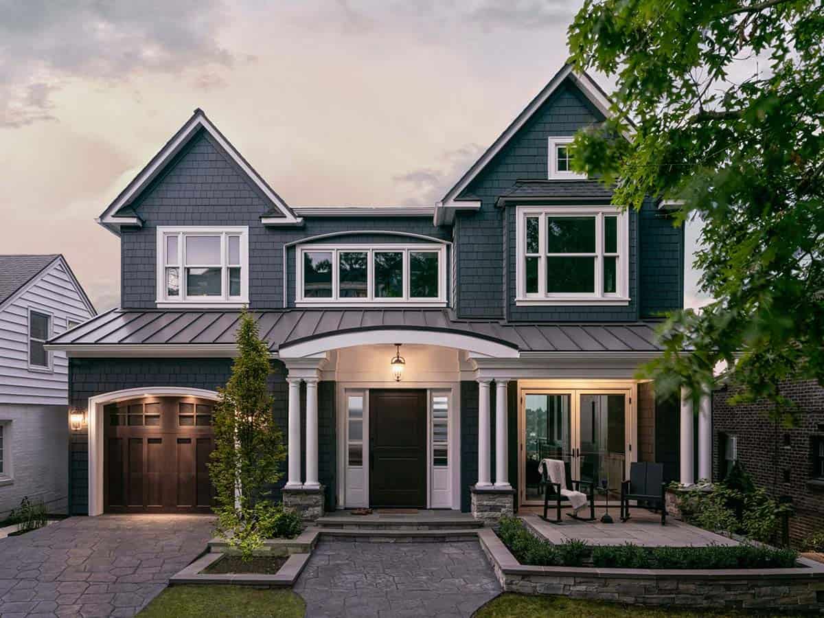 Modern craftsman home front exterior at dusk with lit portico, dark wood garage door, and stone landscaping
