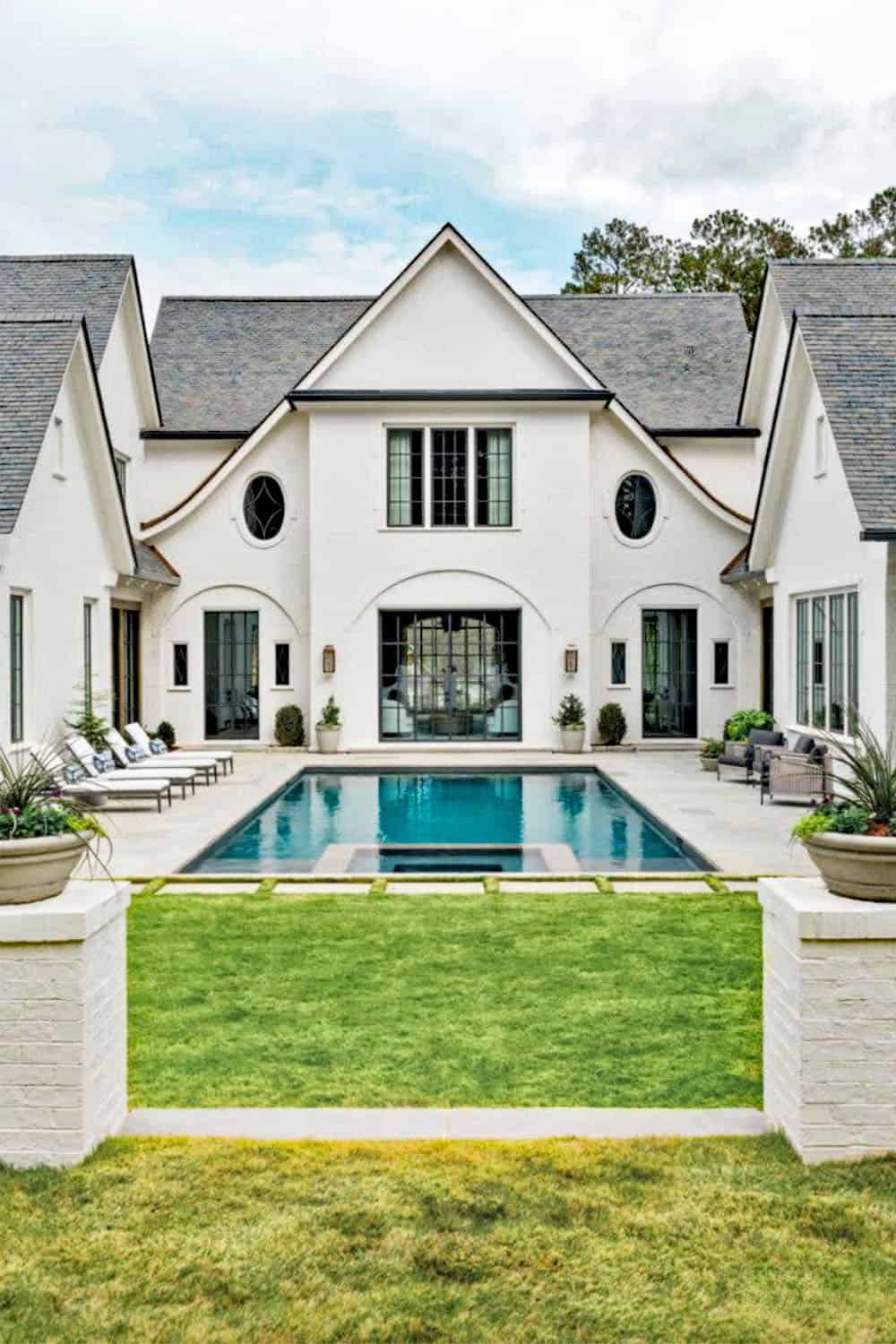 Modern English country house rear exterior with white brick, arched doors, oval windows and rectangular pool in Georgia