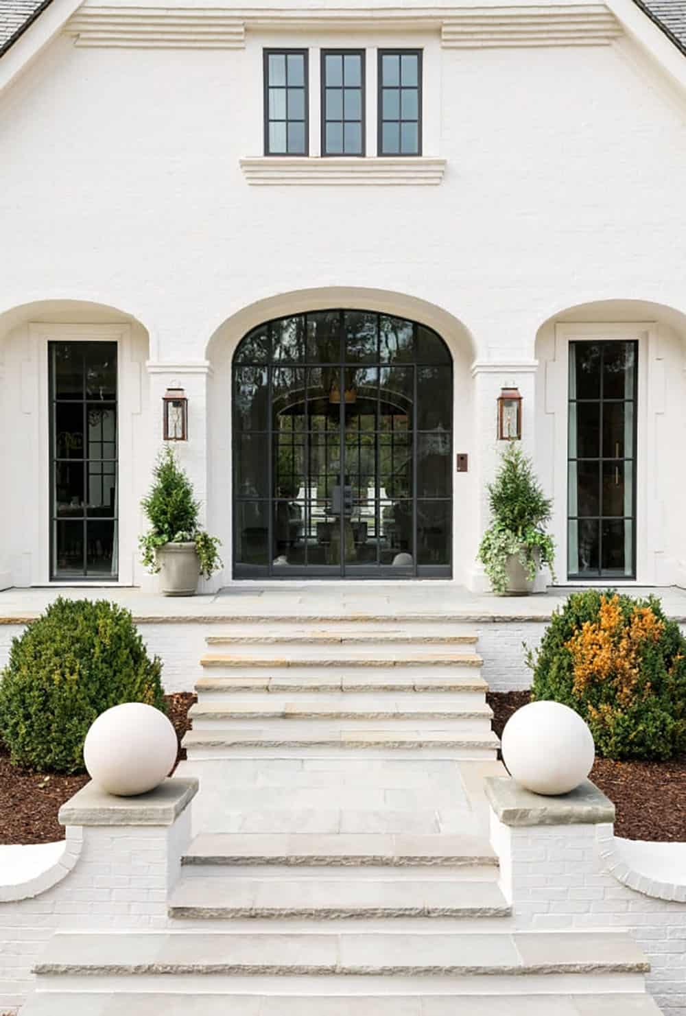 Modern English country house front entry with arched steel-framed doors, stone steps and topiary planters in Georgia