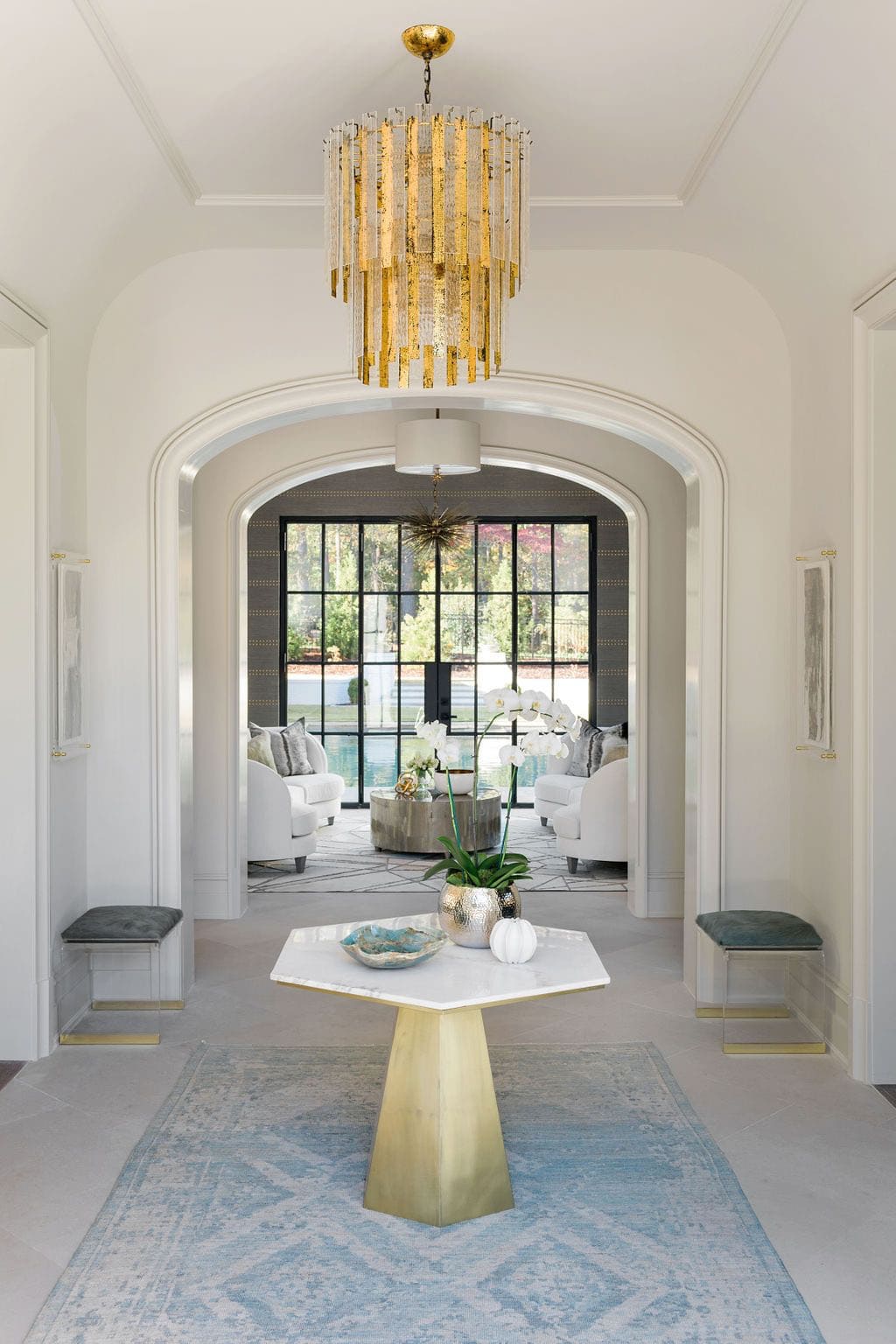 Modern English country house foyer with gold chandelier, hexagonal brass entry table and arched doorway to living room in Georgia
