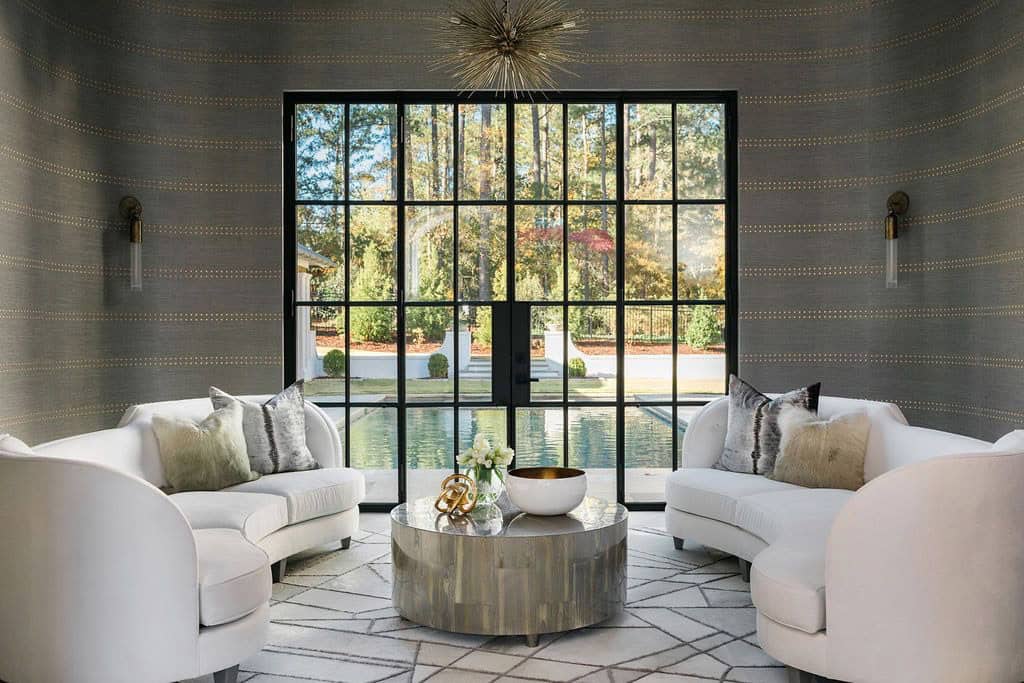 Modern English country living room with curved white sofas, grasscloth wallpaper, Sputnik chandelier and steel-framed pool view in Georgia