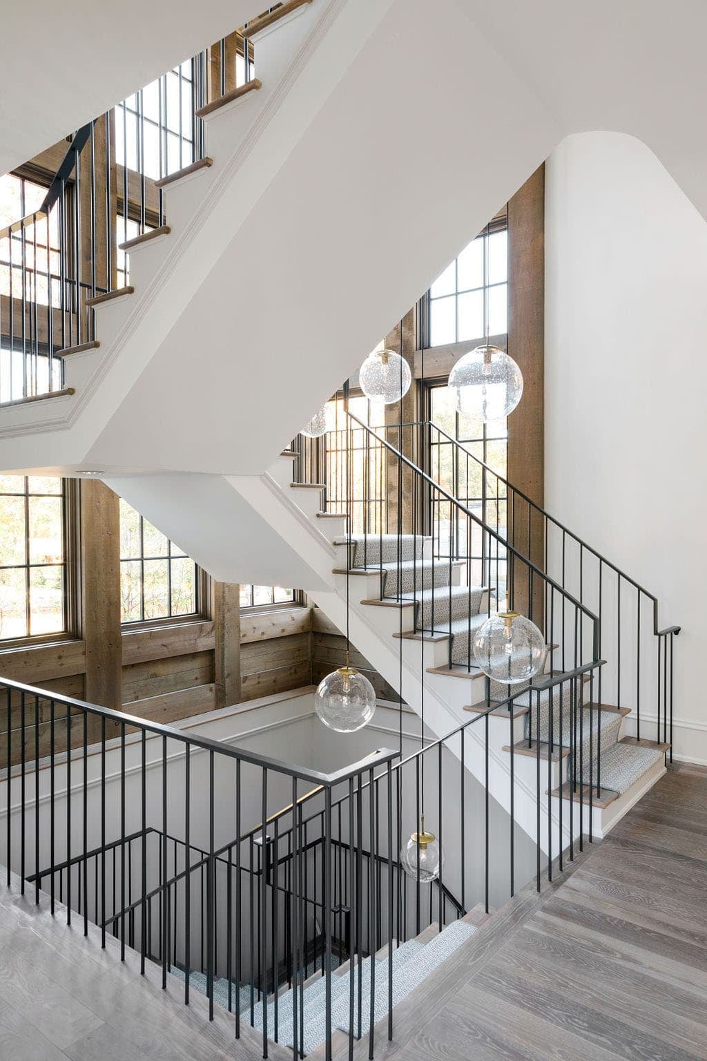Modern English country house floating staircase with black steel railing, globe pendant lights and cedar-framed window wall in Georgia